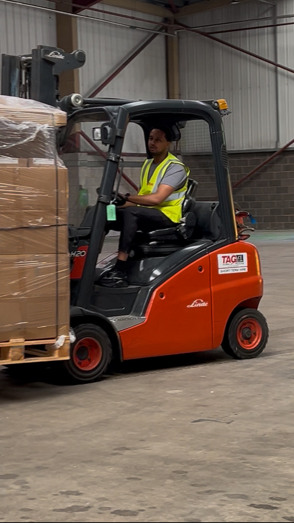 man in a high vis vest operating a forklift carrying a pallet