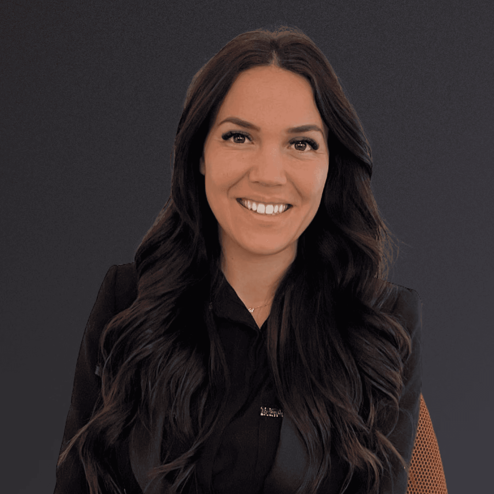 Woman with a short haircut smiling confidently, wearing a blazer and standing in warm natural light with modern architecture behind her.