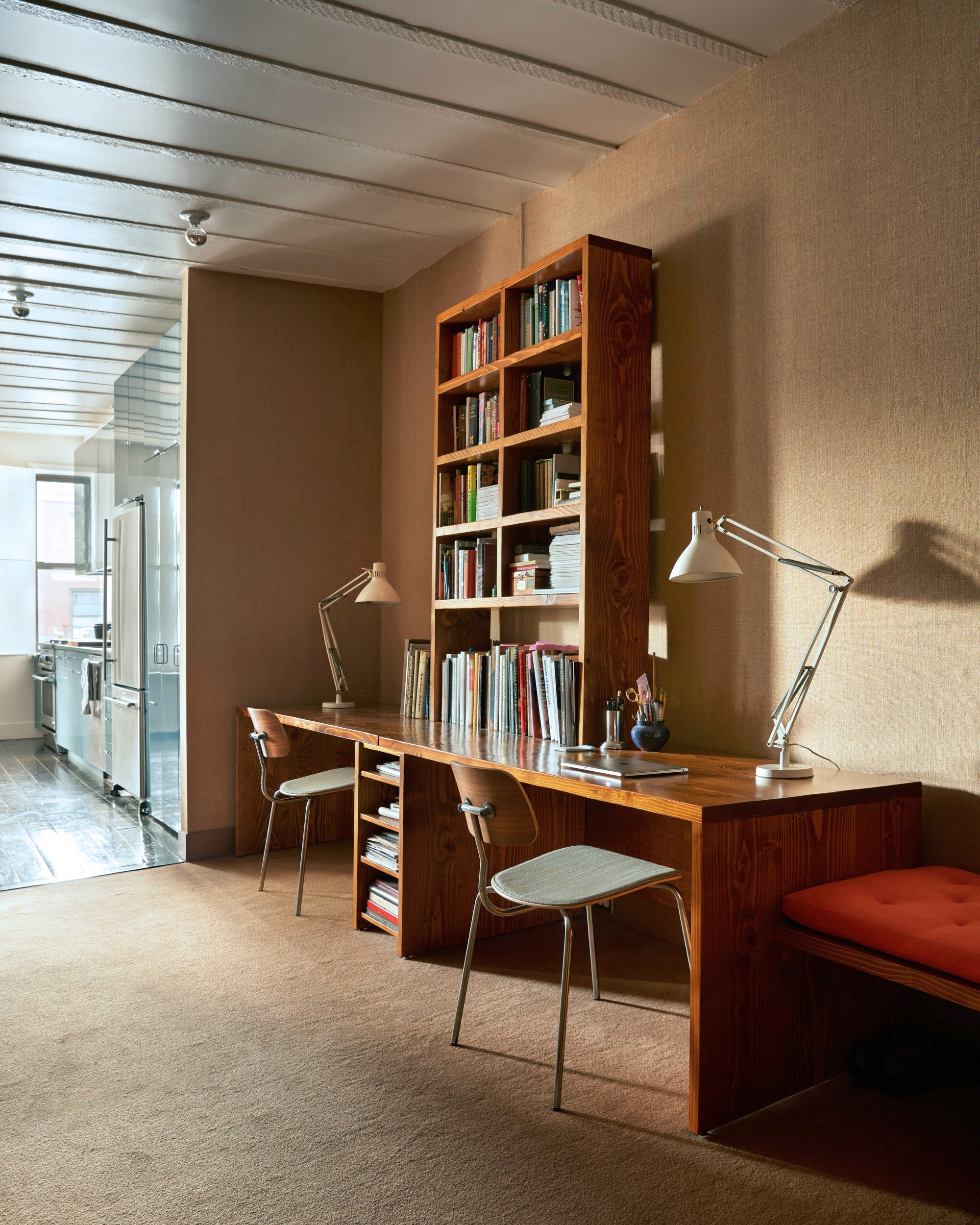 Apartment office with built in desks and bookshelves, vintage table lamps, and a built-in bench with red cushion.