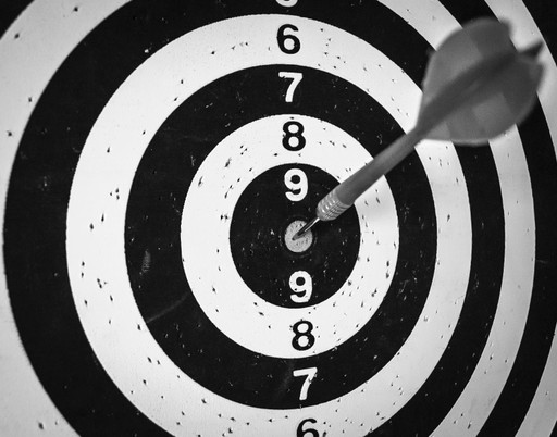 A close-up of a black and white dartboard with an arrow hitting the center.