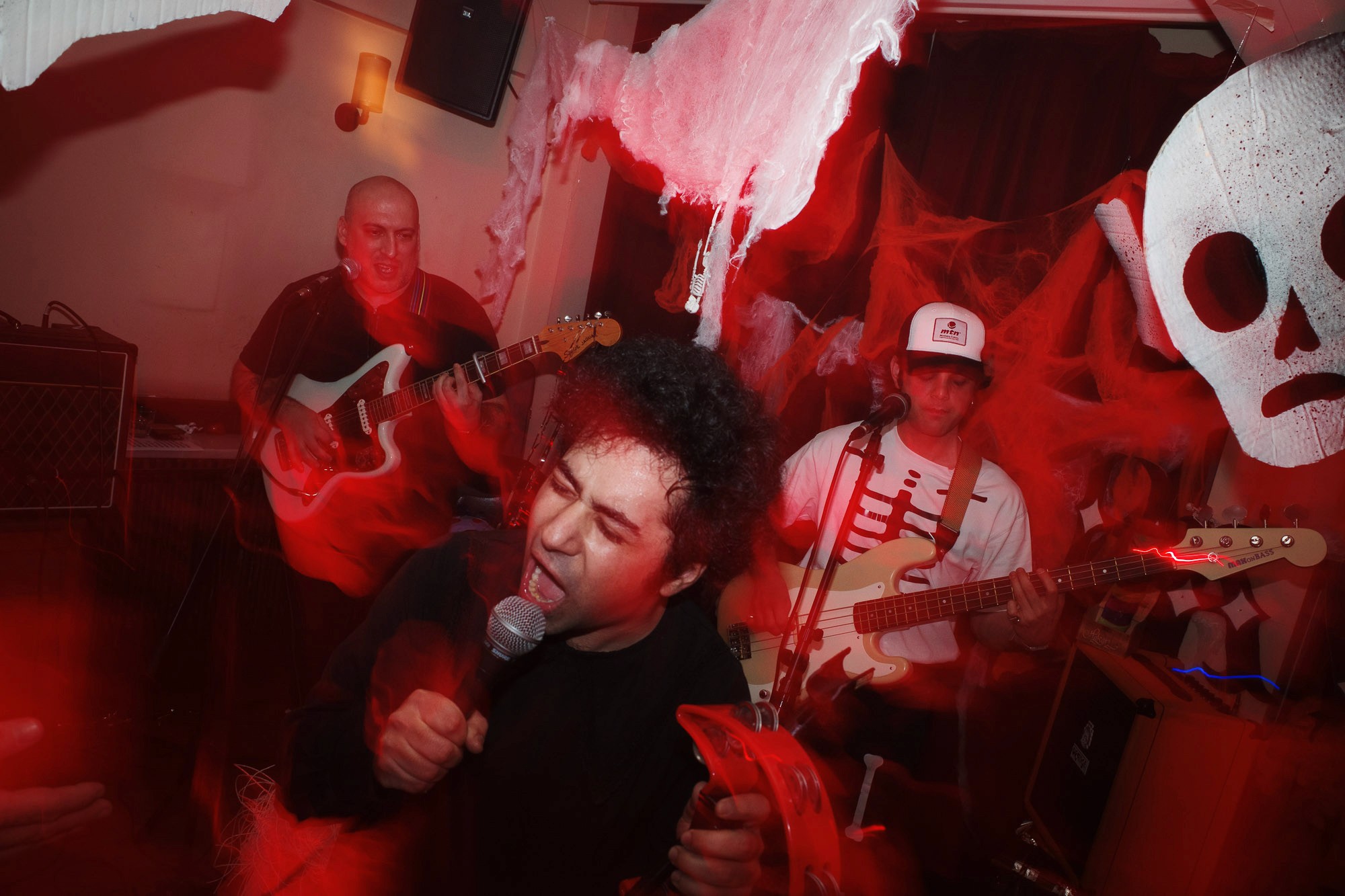 A vibrant Halloween-themed music performance features musicians with guitars playing passionately, surrounded by red lighting and eerie ghost decorations.