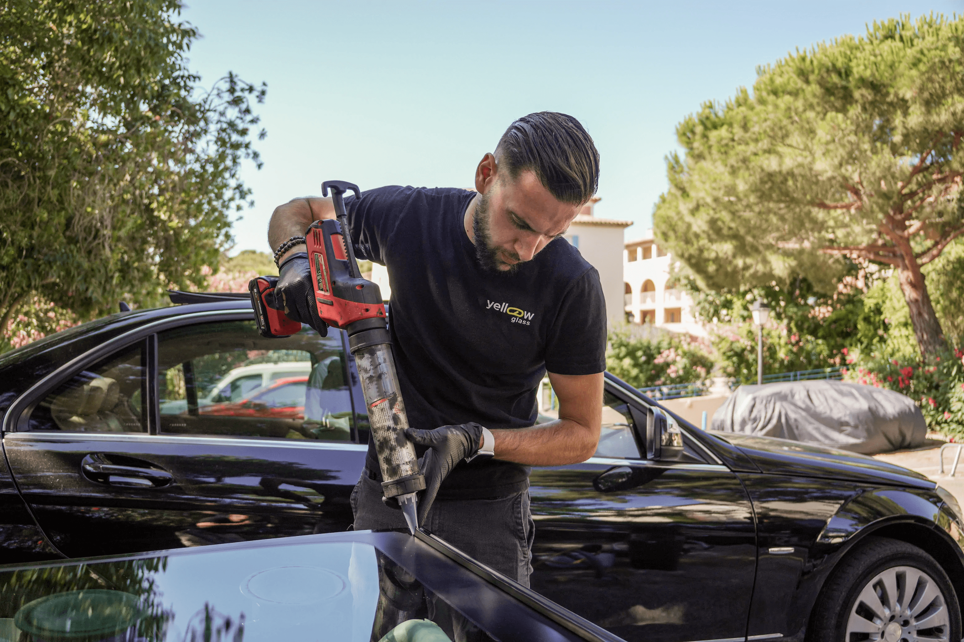 Un technicien remplace le pare-brise d'une voiture noire à l'aide d'un pistolet à mastic. Réparation automobile professionnelle.
