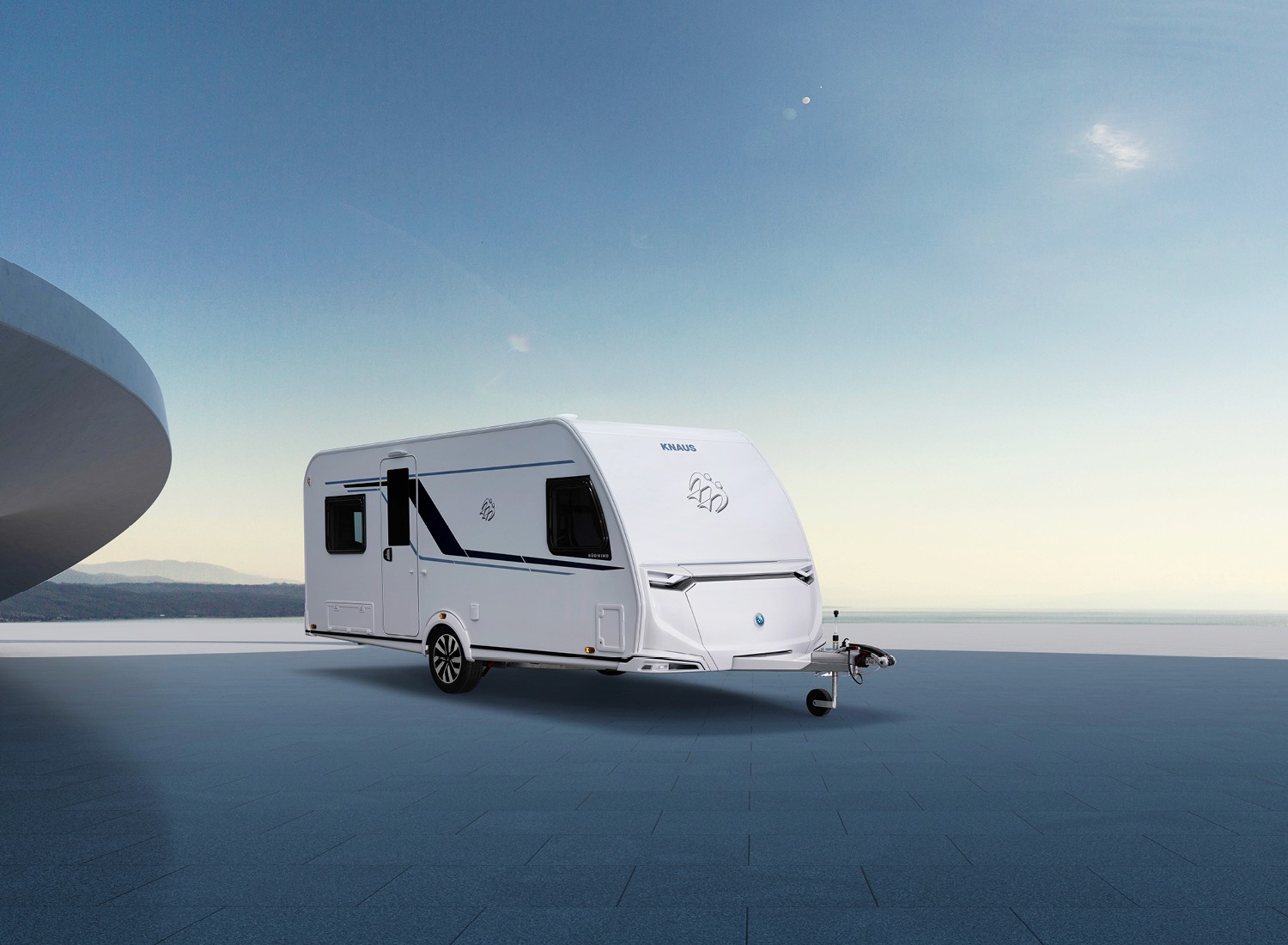 Ein moderner KNAUS Wohnwagen steht auf einer weiten, gepflasterten Fläche mit Blick auf den Horizont und den Himmel in kühlem Morgenlicht.