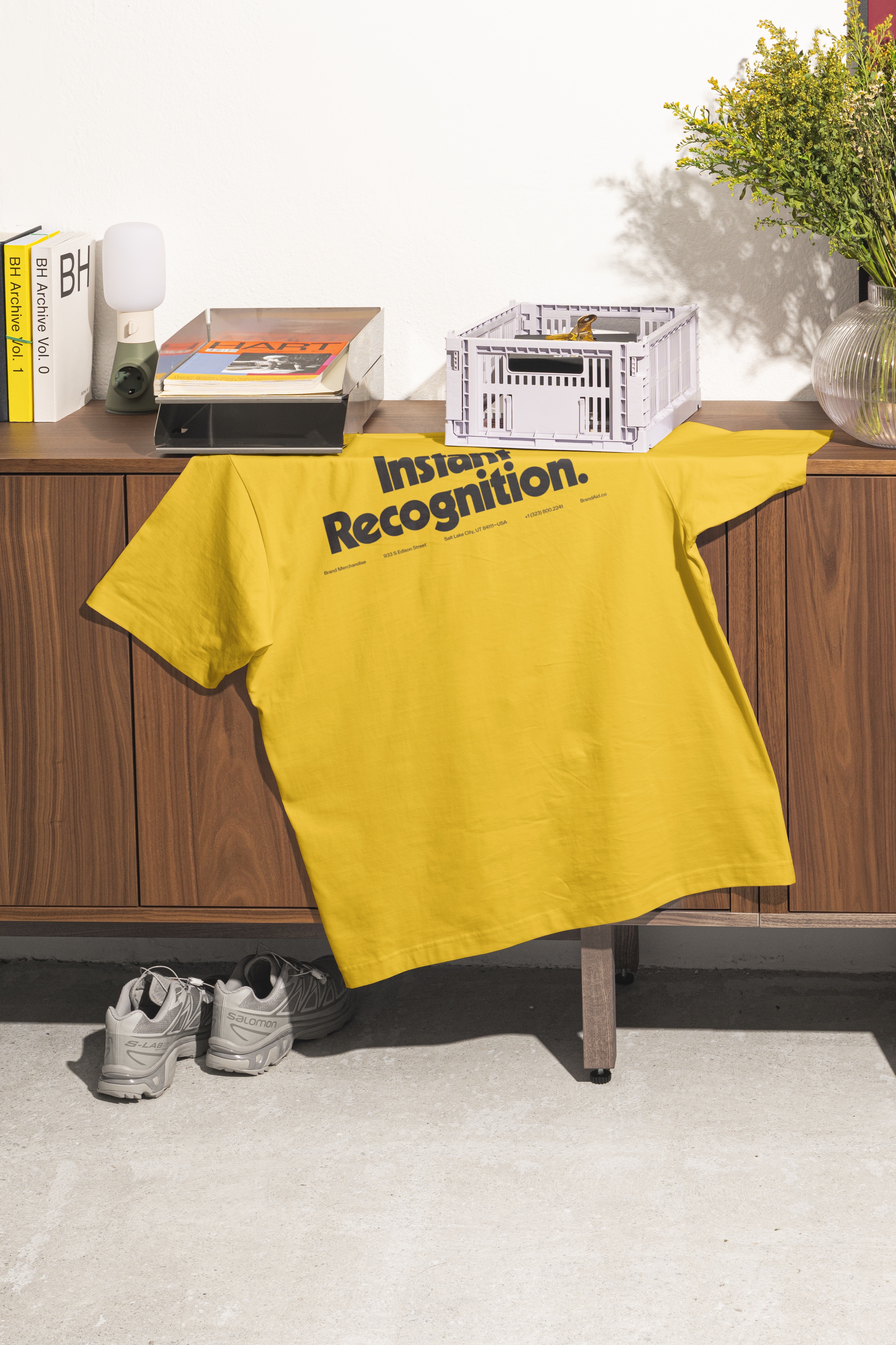 A bright yellow T-shirt hangs casually on a wooden cabinet, with some weights and plants nearby.