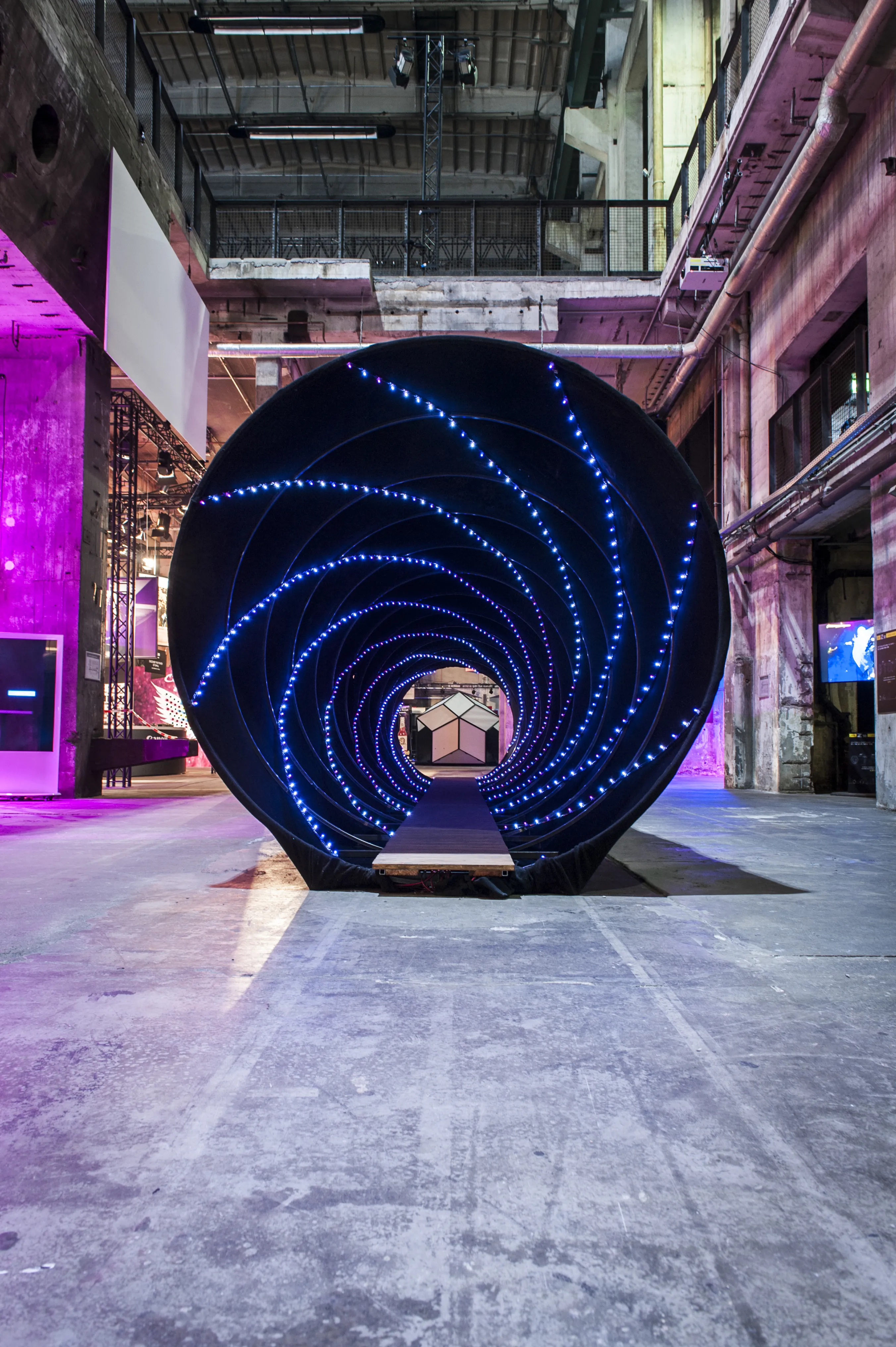 Walk-through black spiral tunnel with rings of blue LED lights at BERLIN PHOTOWEEK in the Kraftwerk industrial hall.