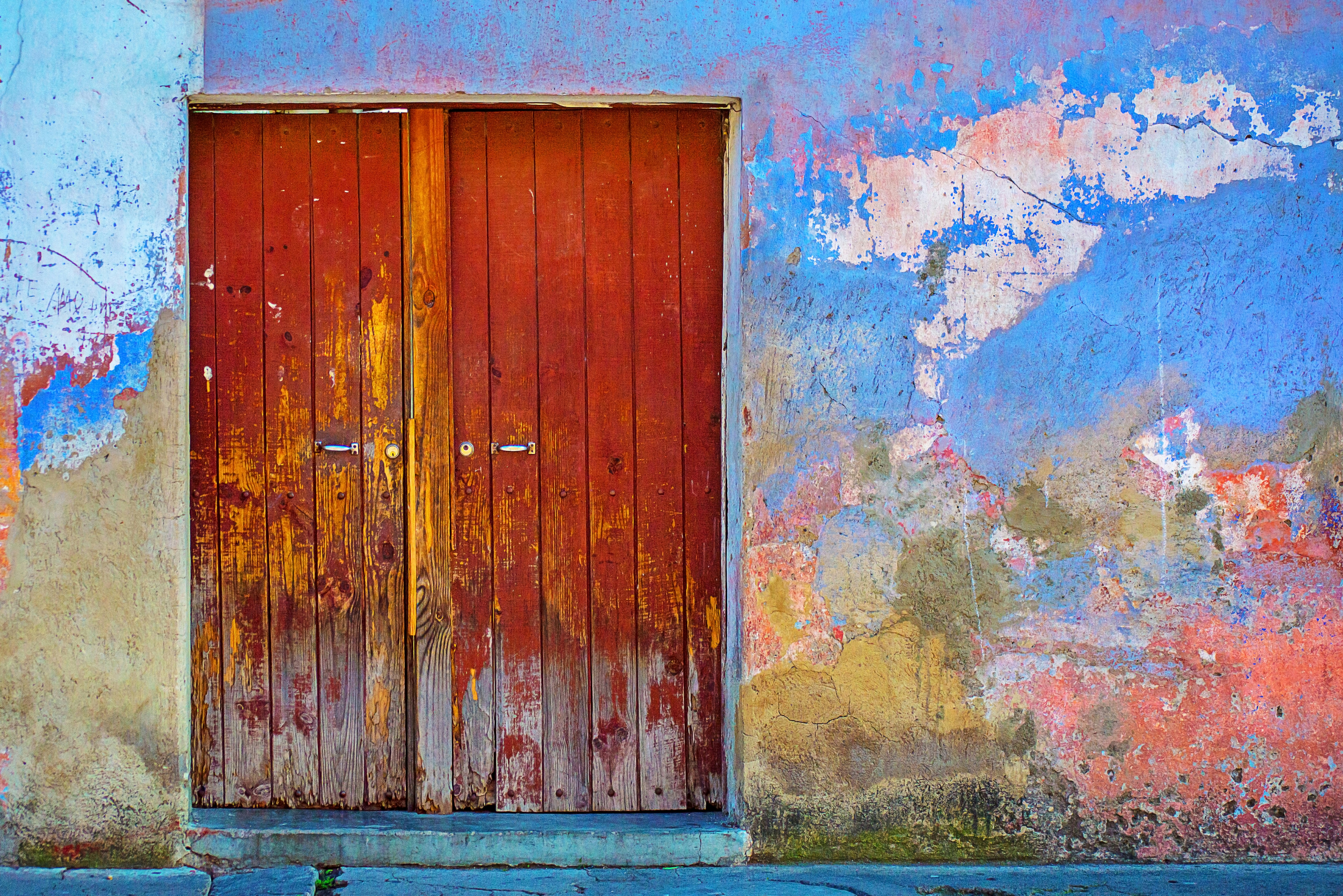 A vibrant, weathered wooden door stands against a colorful, textured wall with peeling paint, featuring shades of blue, red, yellow, and orange, evoking a rustic, artistic ambiance.