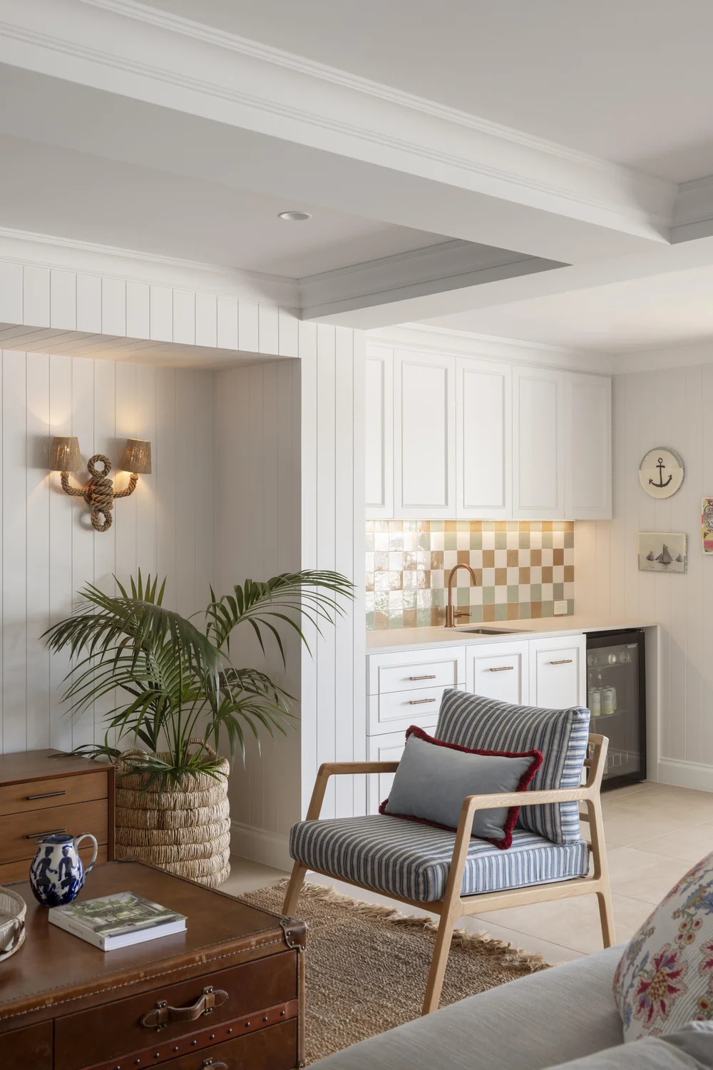 Living area with armchair, built-in kitchenette, and tiled splashback detail.