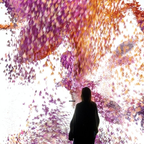 一个人站在面前的绚丽数字显示屏前，屏幕上呈现着紫色和橙色的旋转图案。