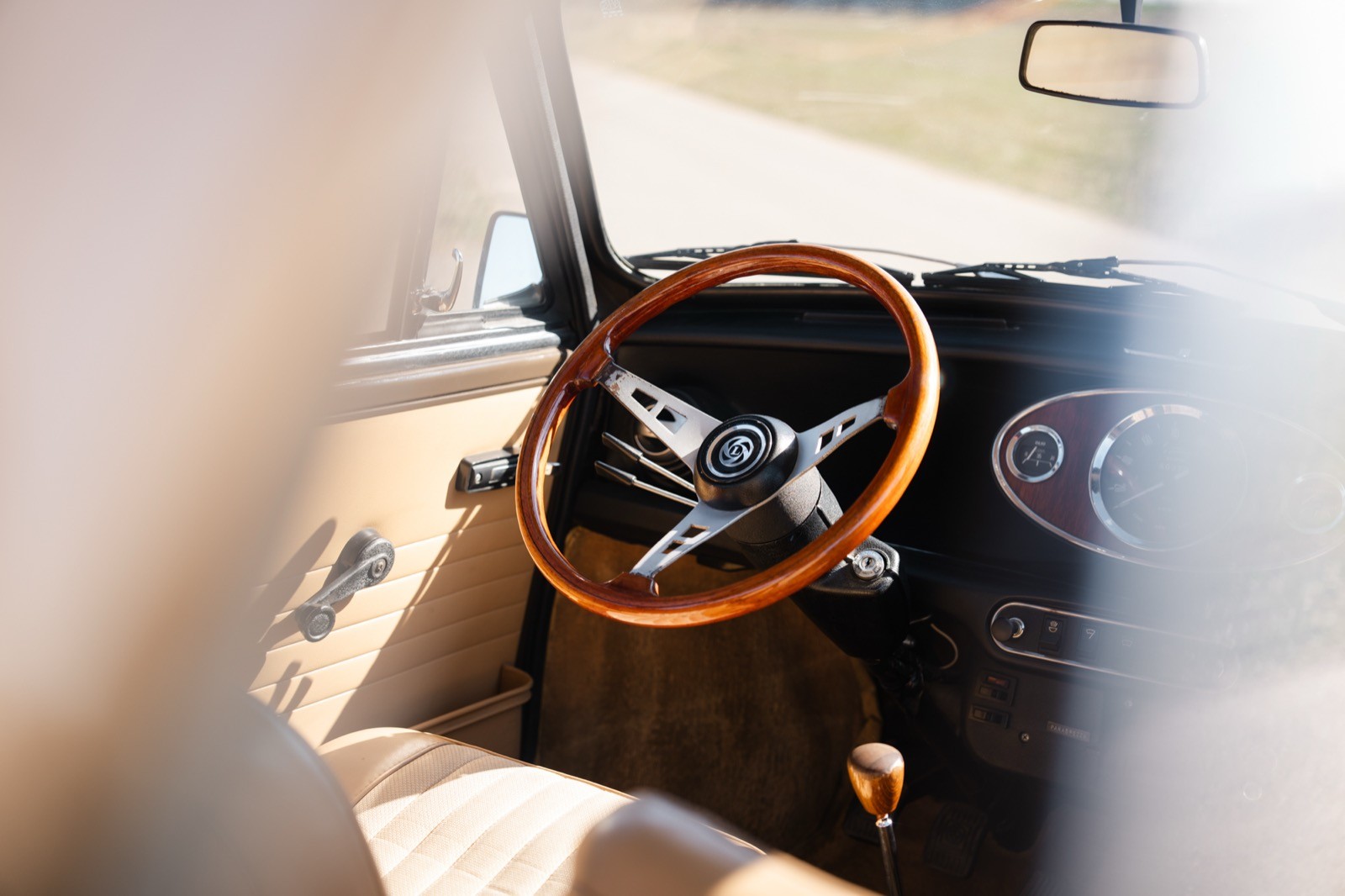 Close-up of a car’s interior featuring a wooden steering wheel and dashboard with sunlight streaming in.