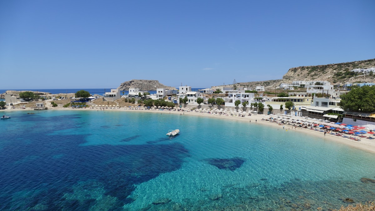 Clear turquoise water along a sandy Greek island beach lined with white buildings