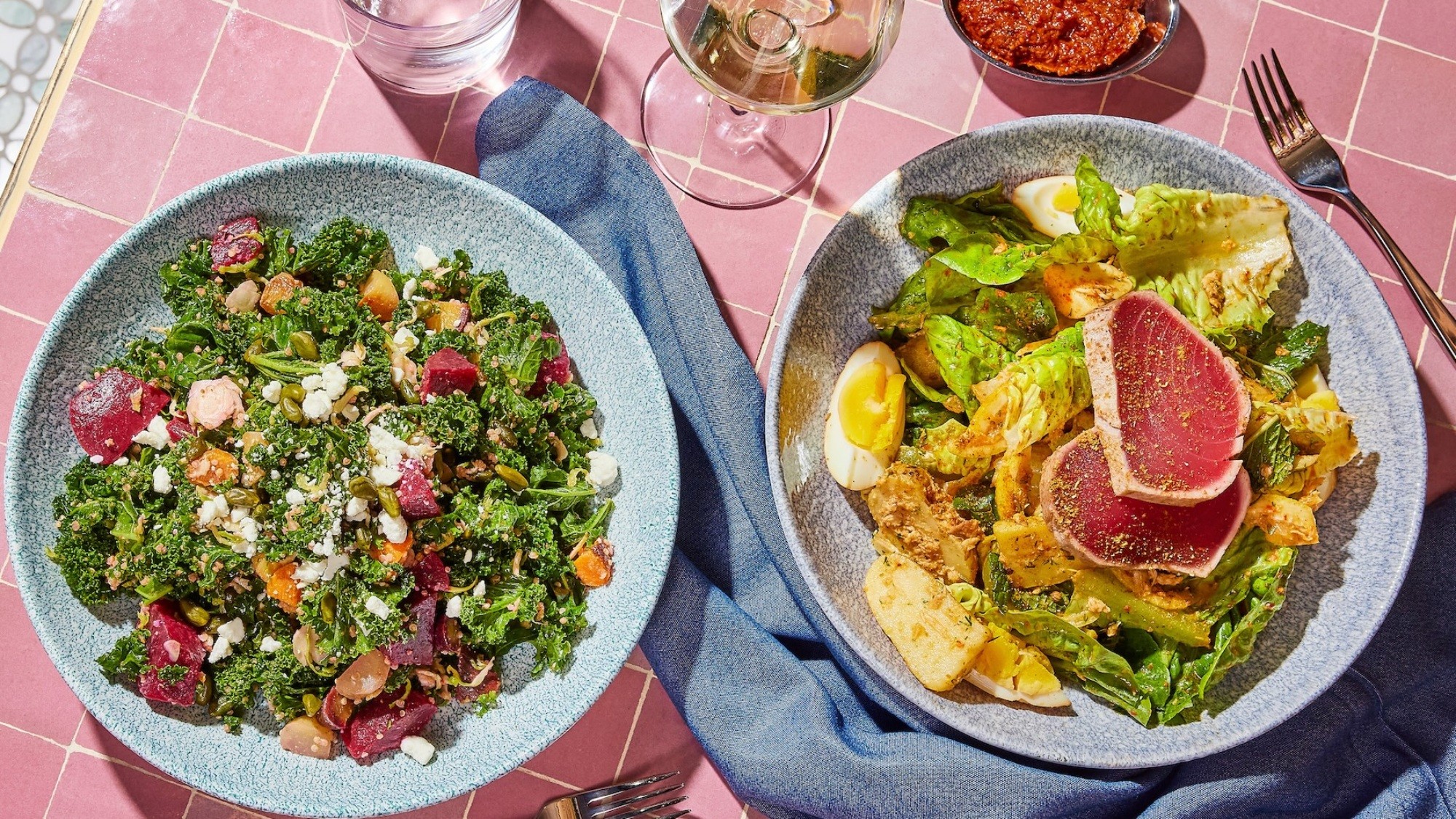 Professional food photography of two gourmet salad bowls on pink tile background — kale and beetroot salad with feta and pumpkin seeds alongside seared tuna nicoise — F&B photography by Makers' Studio Bahrain