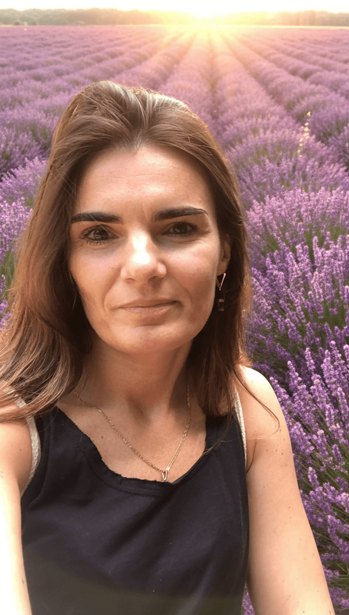 Smiling female therapist with short gray hair, wearing a brown top and a purple shawl, surrounded by a cozy background.