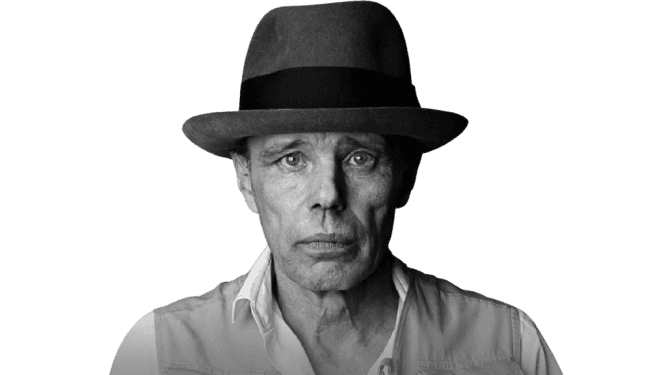 A striking black-and-white portrait of a man wearing a wide-brimmed fedora, staring directly at the camera with a serious, introspective expression. His rugged features and the minimalist background create a stark, artistic feel, while his casual attire, featuring a collared shirt and vest, contrasts with the formality of his hat. The image evokes a sense of individuality and depth.