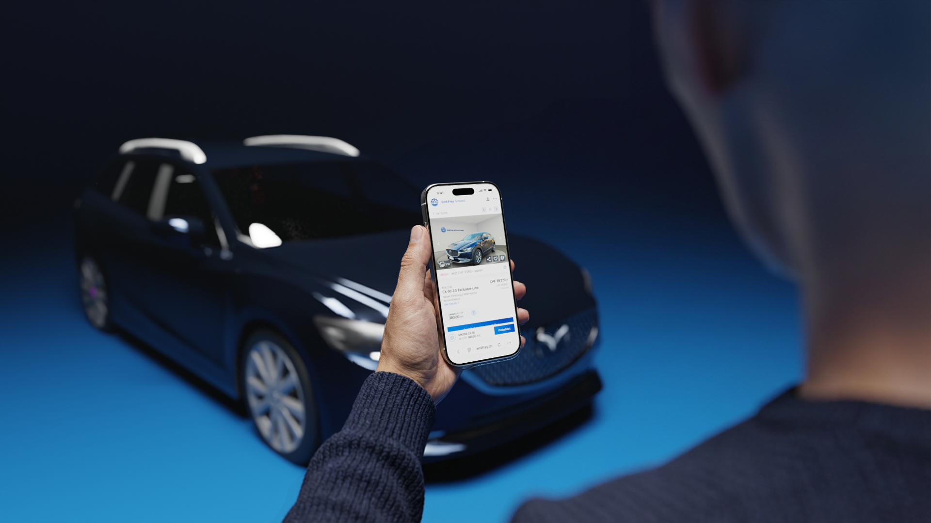 Eine Person hält ein Handy in der Hand, auf dessen Display die Website von Emil Frey Switzerland zu sehen ist. Hinter dem Handy steht ein Automodell, das genau dem auf dem Handy abgebildeten Modell entspricht. 