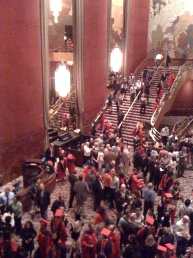 A photo of a hallway with stairs where multiple people and graduate students interact with each other.