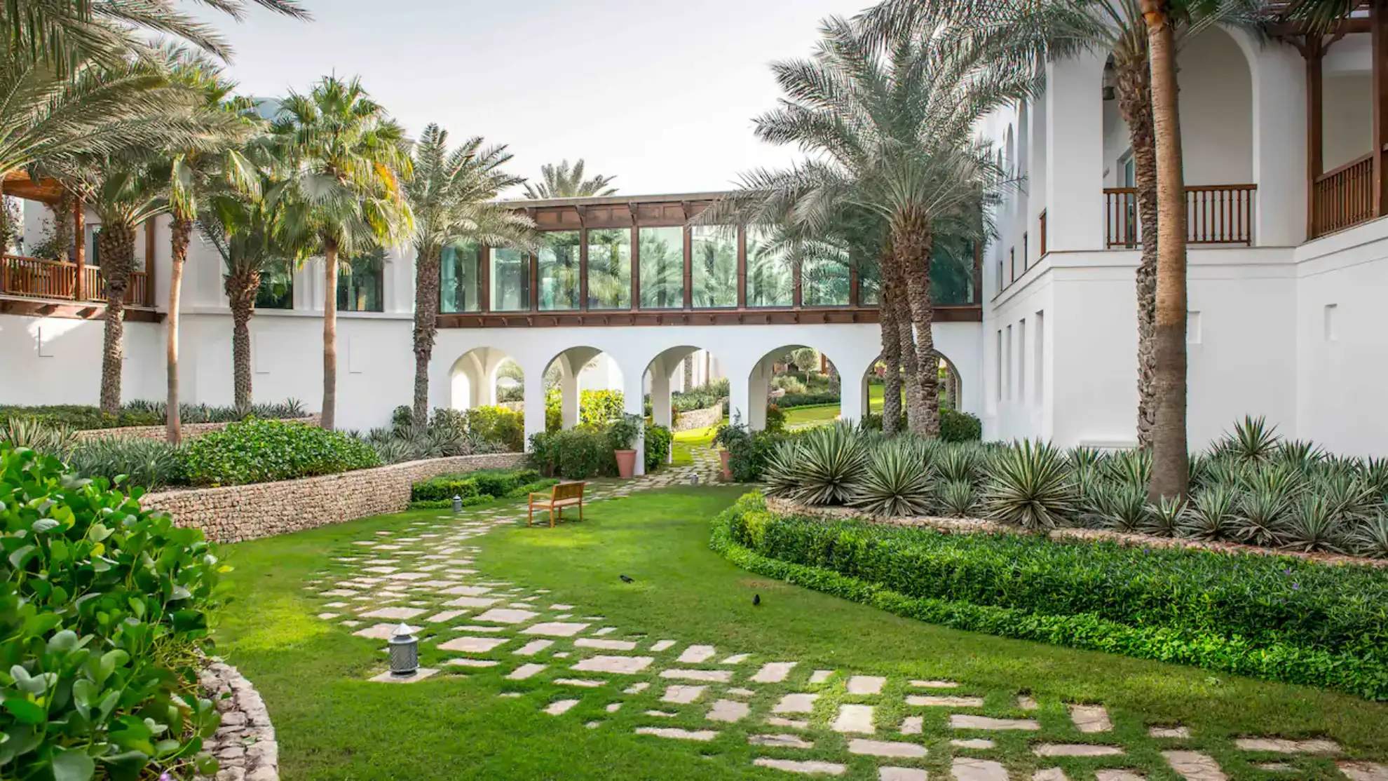 Park Hyatt Dubai with lush landscapes, palm trees, a walkway, and white structures.