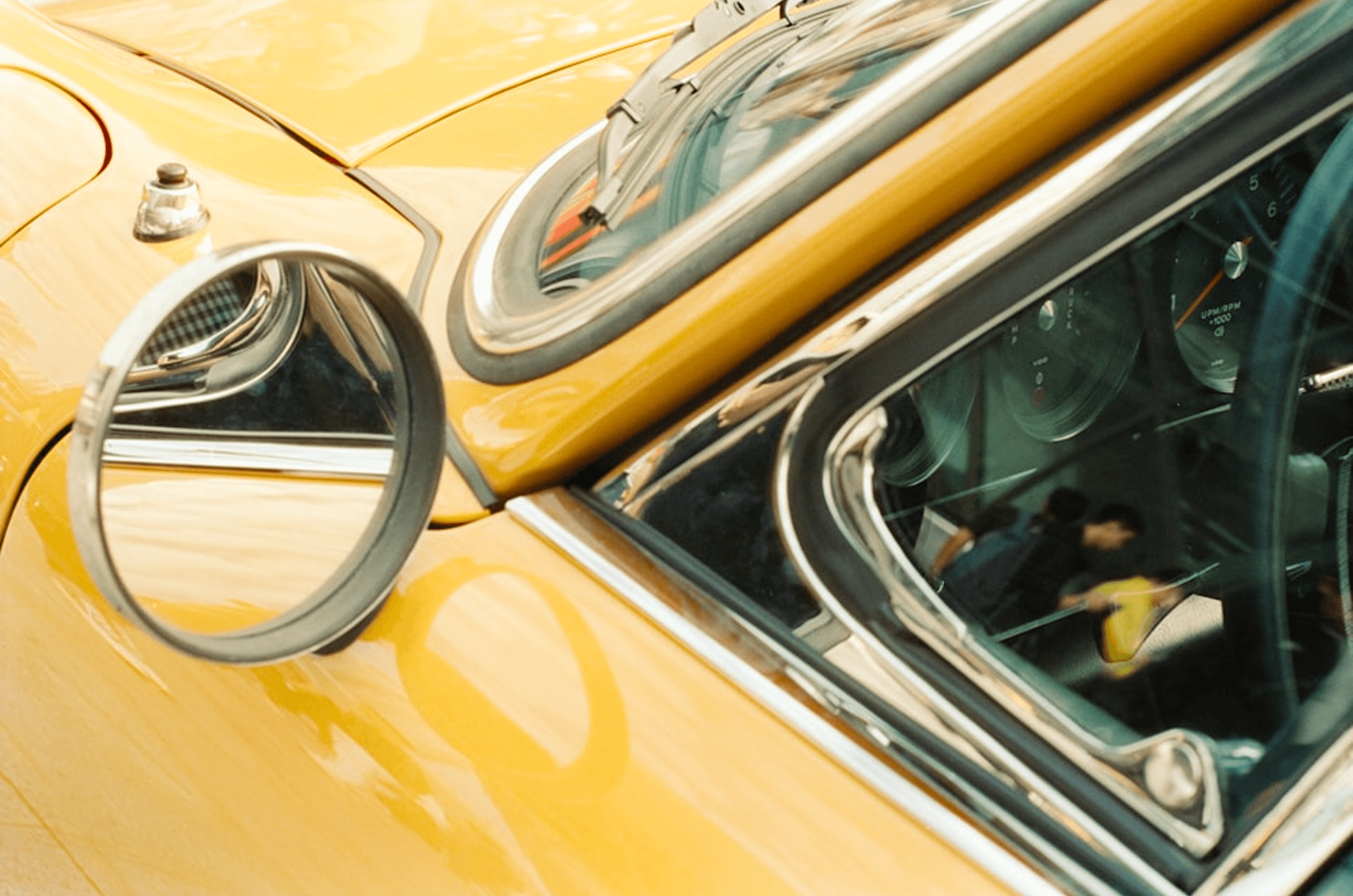 Close-up of a yellow vintage sports car showing side mirror, window, and dashboard details through the glass