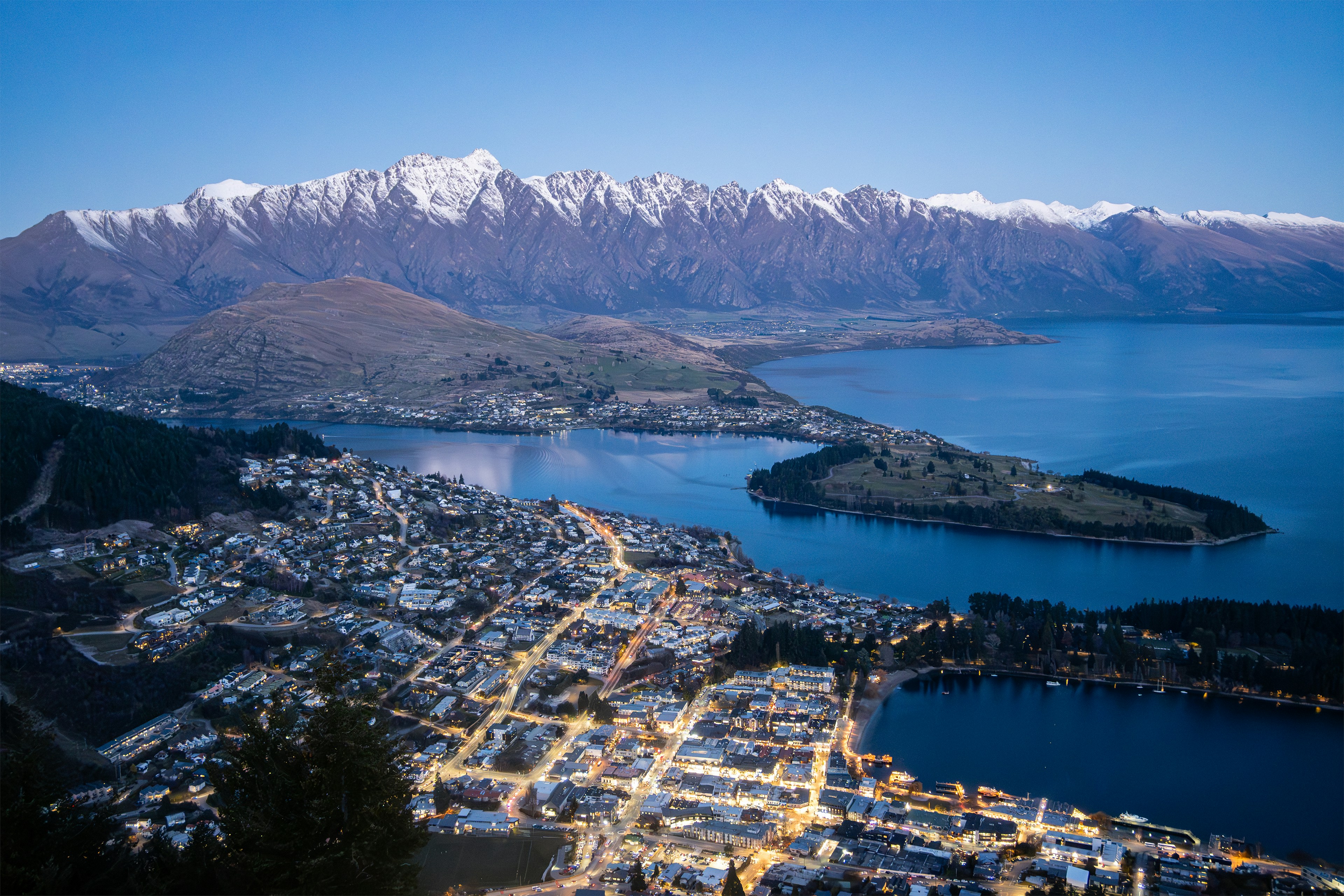 Snow-capped mountains overlook a coastal town at dusk.