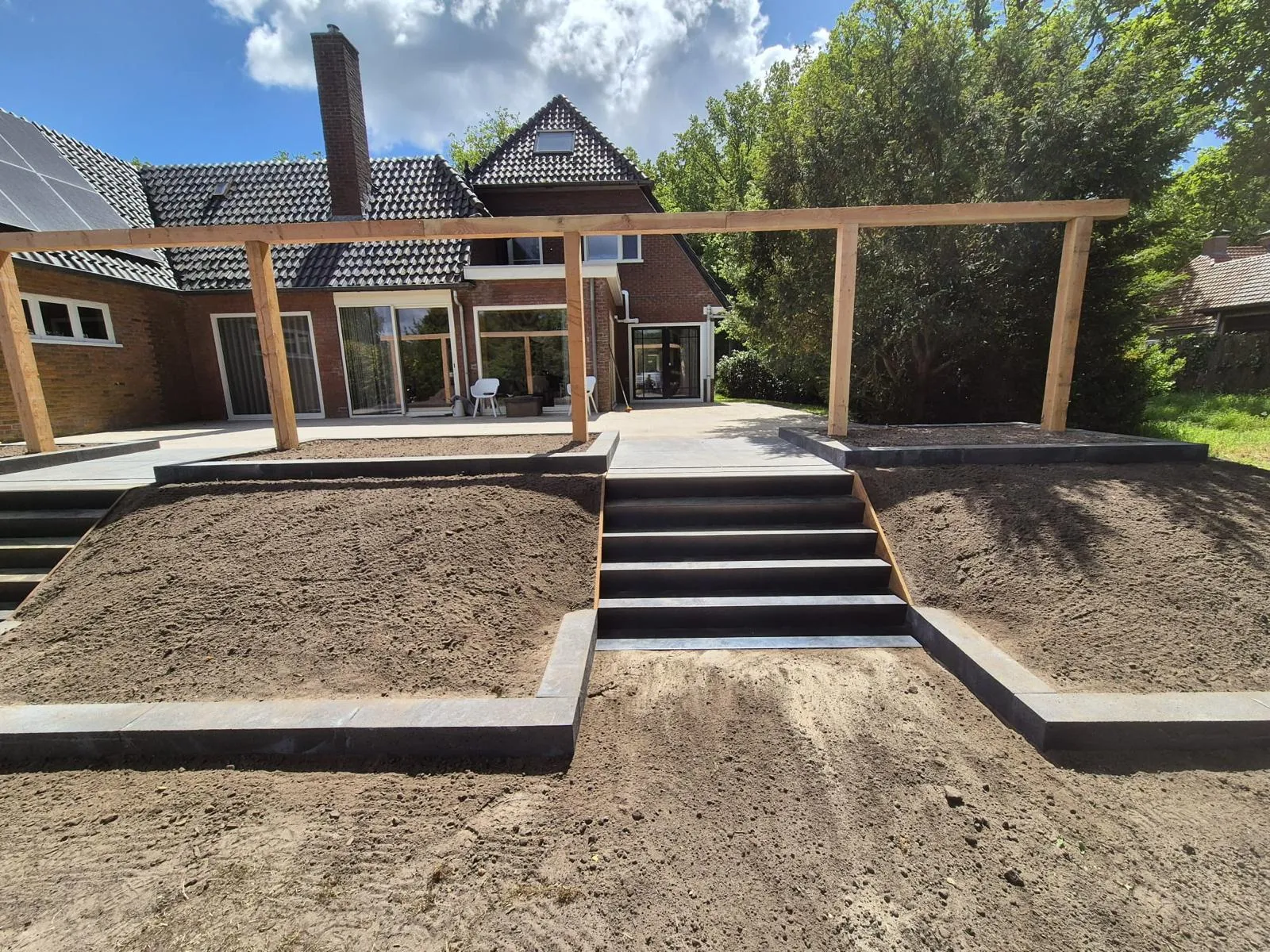 Brede traptreden, paalfundering en zandbed in tuin in aanbouw, voorbeeld van zorgvuldige tuinaanleg in Friesland