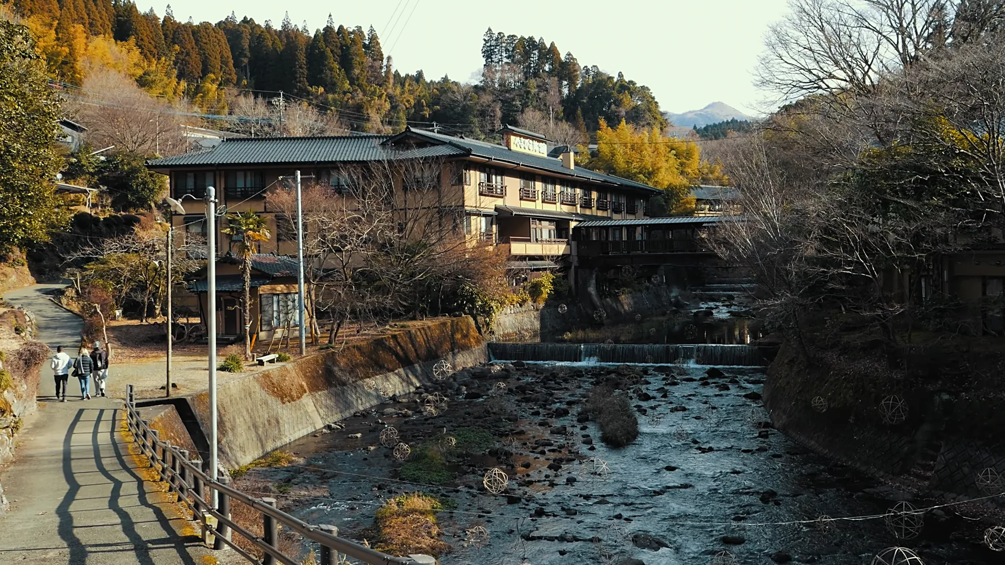 Walkers on the riverside walkway past an inn at Kurokawa Onsen