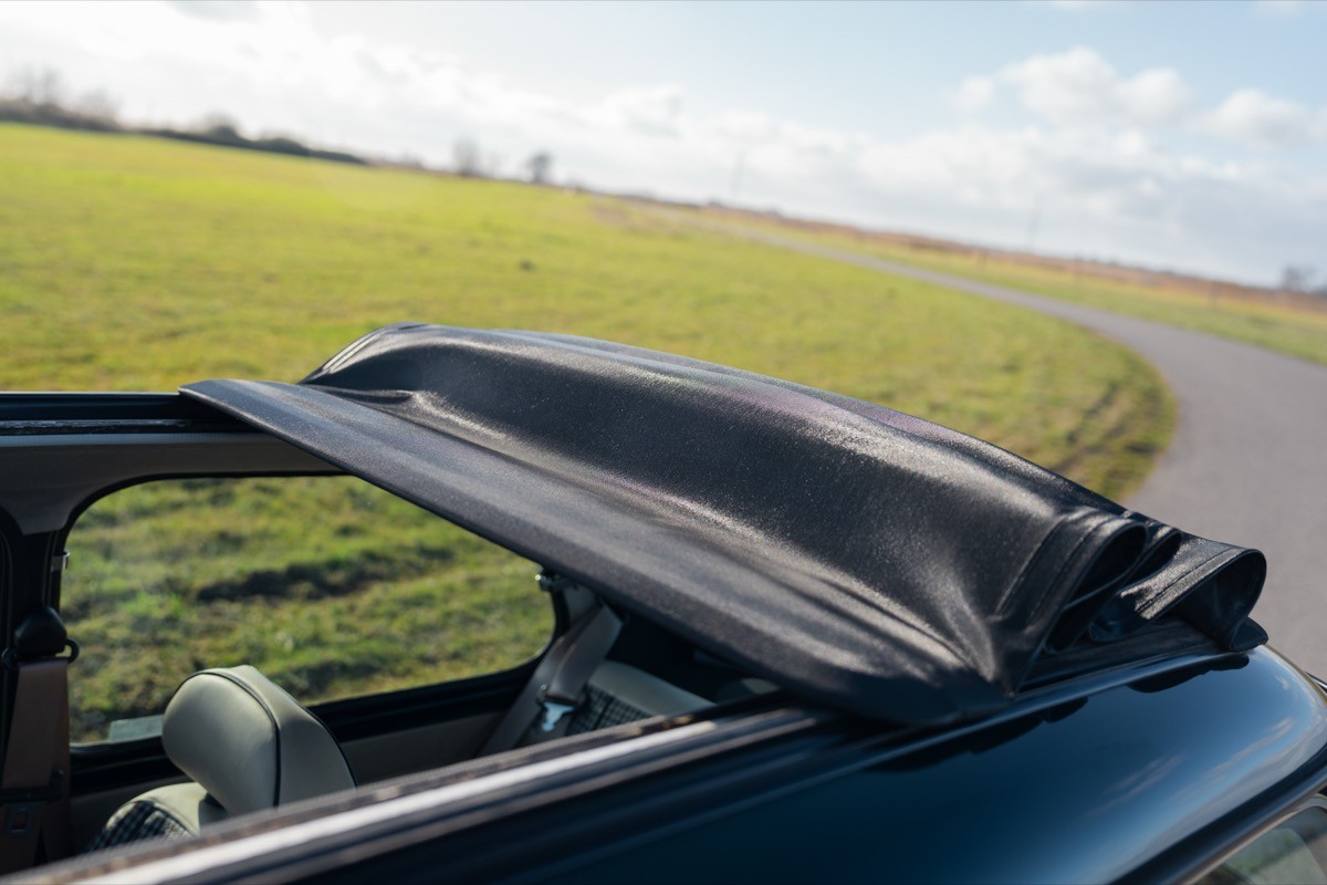 A close-up of a car's open sunroof, with a green field and blue skies in the background.