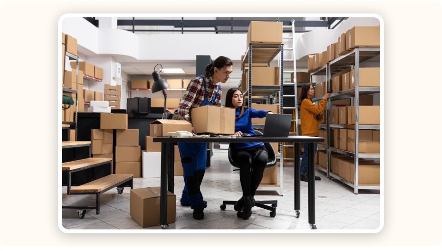Warehouse workers packing boxes while coordinating orders on laptop and shelves