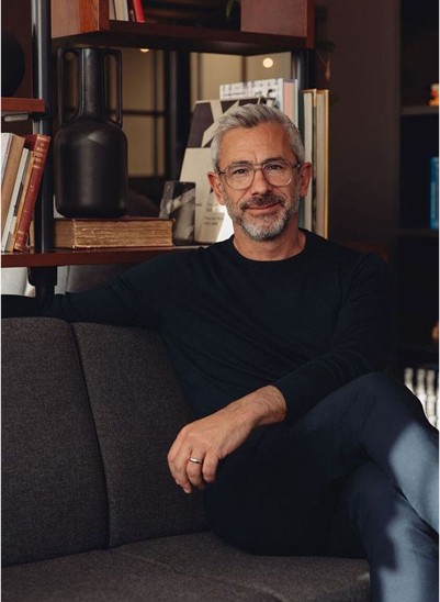 Senior man with gray hair and glasses smiling on a sofa.