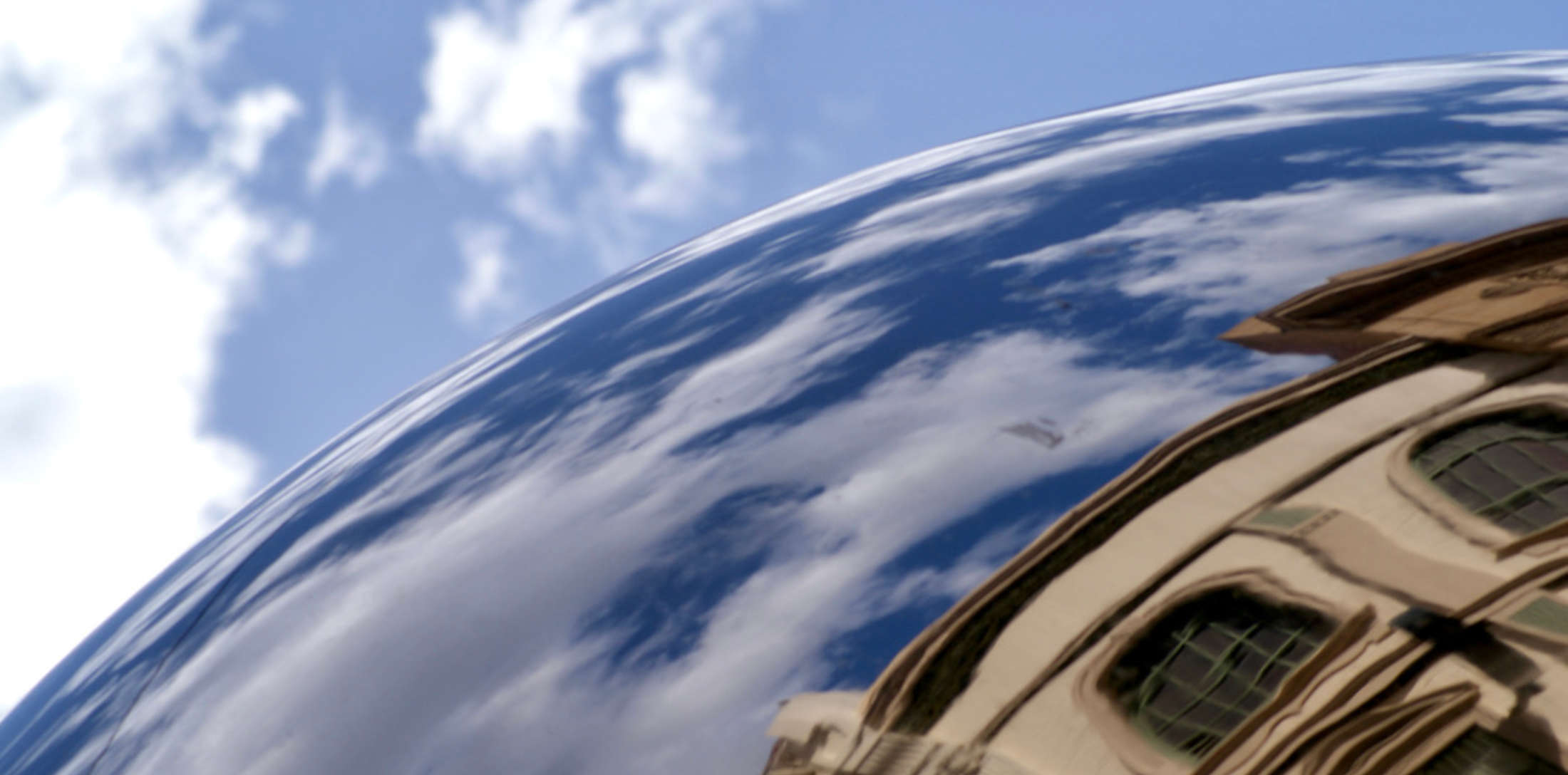 A spherical mirror in Adelaide, reflecting the blue sky, clouds and surrounding buildings. It looks like a small planet.