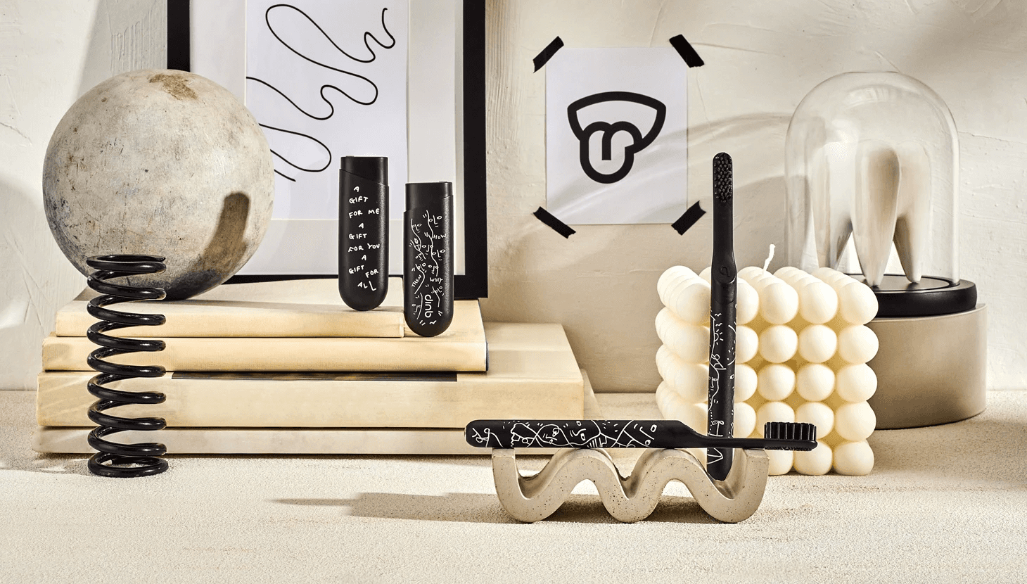 Black toothbrushes and travel covers with white line drawings, styled among books, a sphere, a spring and a bubble candle