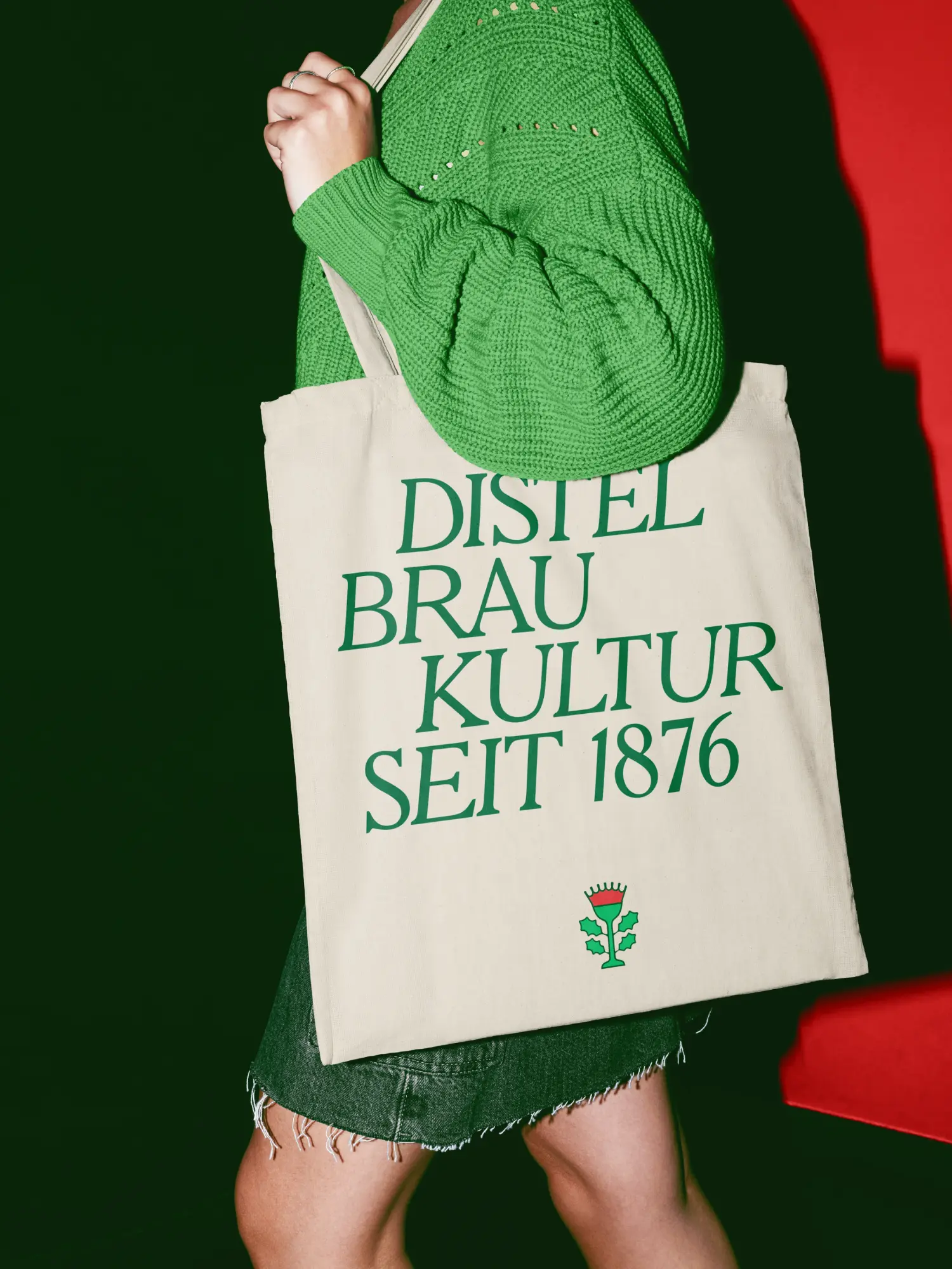 Person mit grünem Pullover und Stofftasche mit Aufschrift „Distel Braukultur seit 1876“