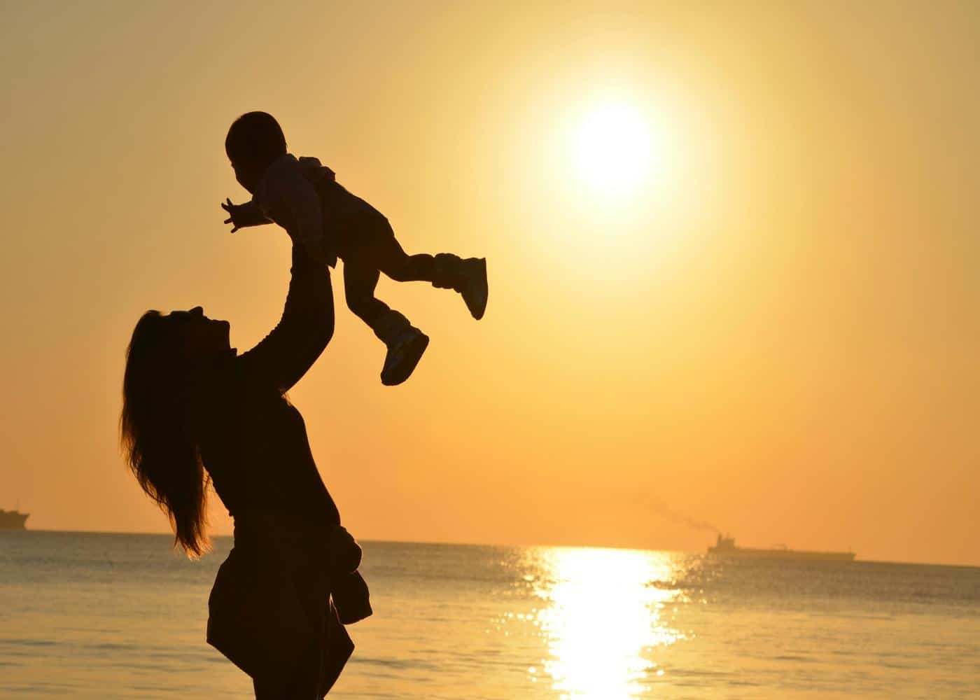 Silhouette of a woman throwing her baby in the air against a sunset backdrop