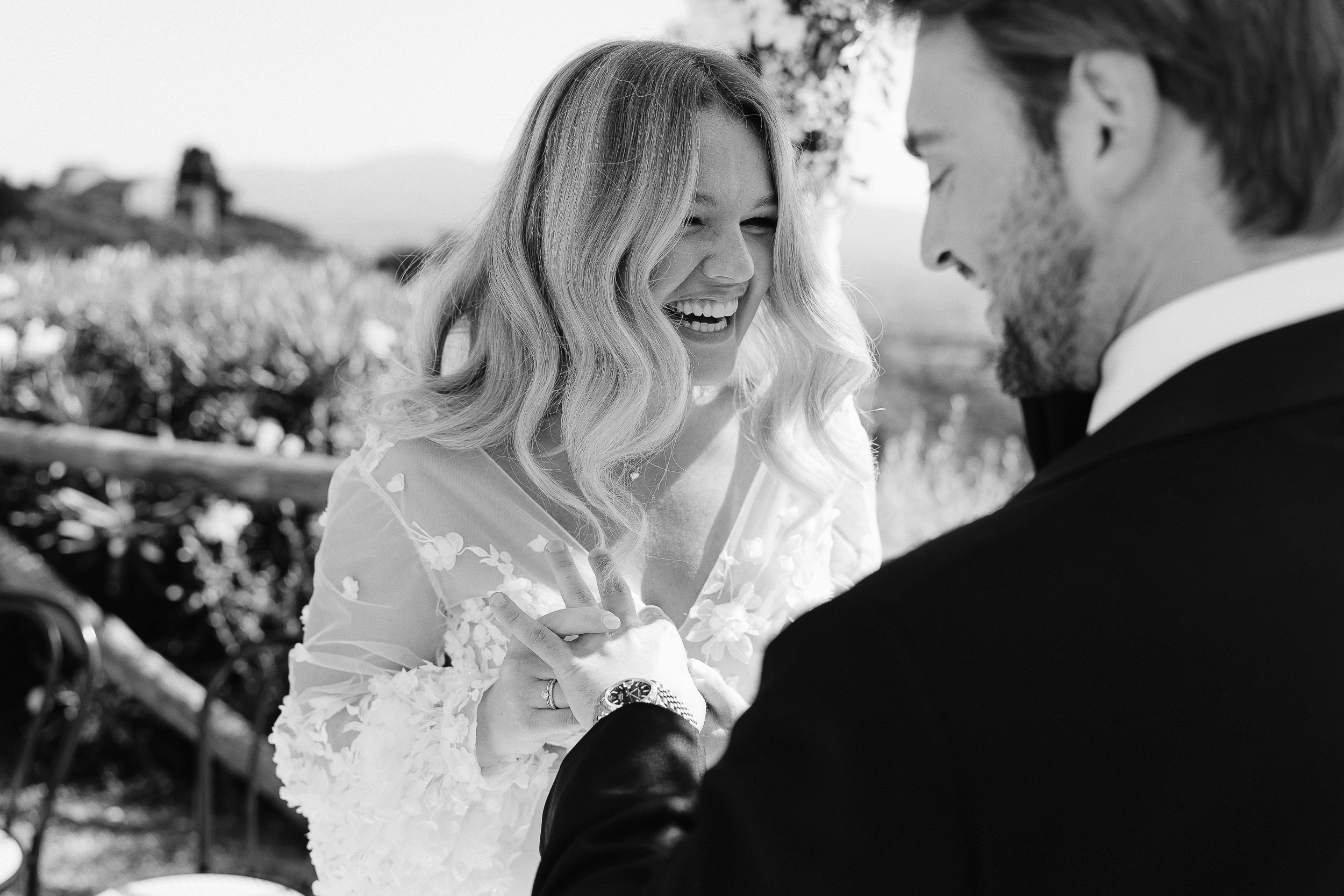 A bride and groom share a tender moment, smiling and embracing in a romantic outdoor setting.