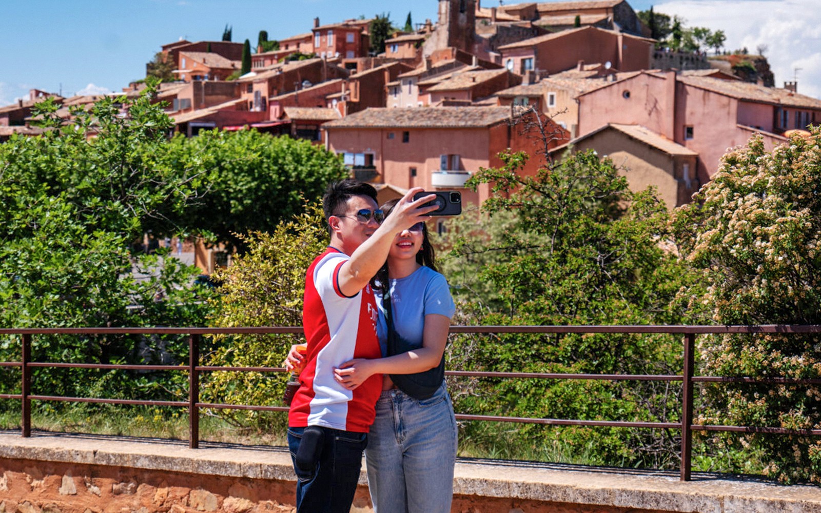 Couple taking a selfie with the colorful village of Roussillon, Provence in the background.