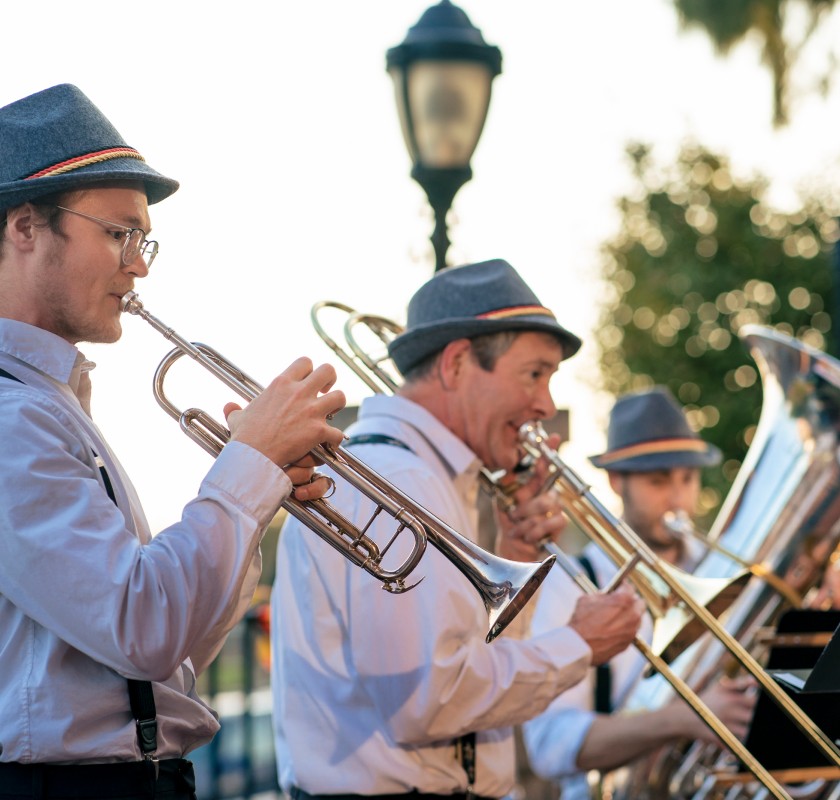 Three brass musicians playing outdoors, wearing Bavarian-style hats.
