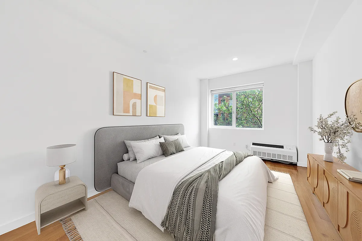 A cozy bedroom featuring a bed, a nightstand, and a window allowing natural light to enter the space.