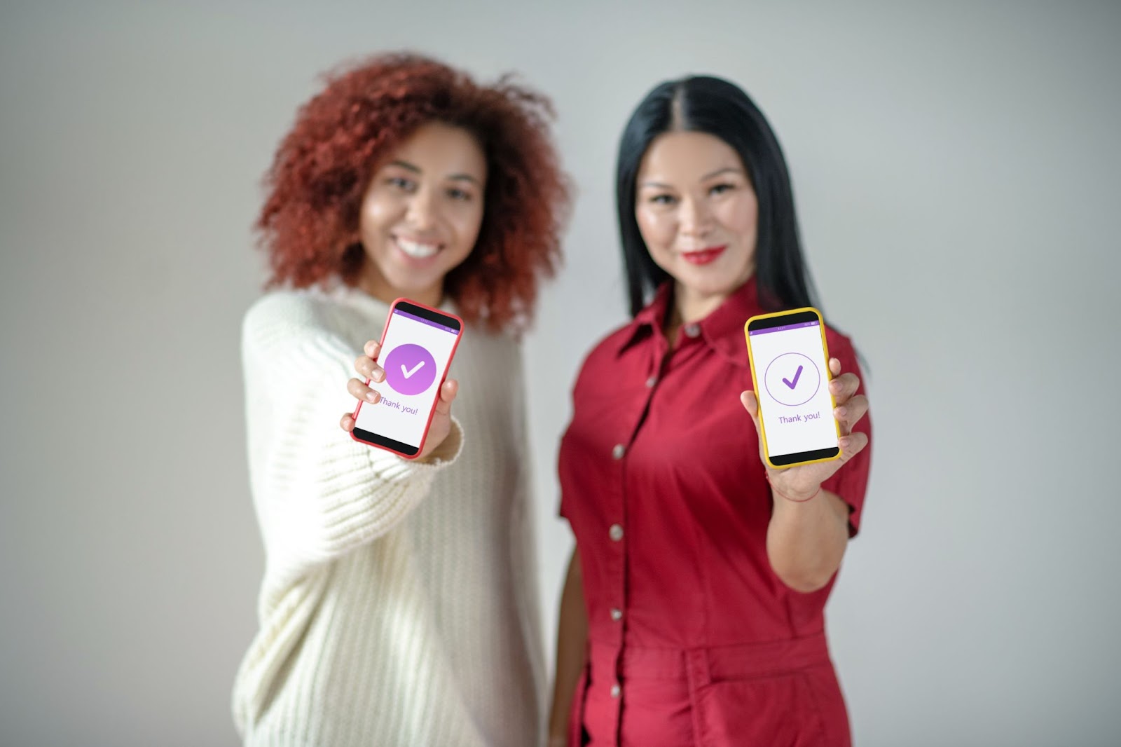 Two women holding up their cell phones. 