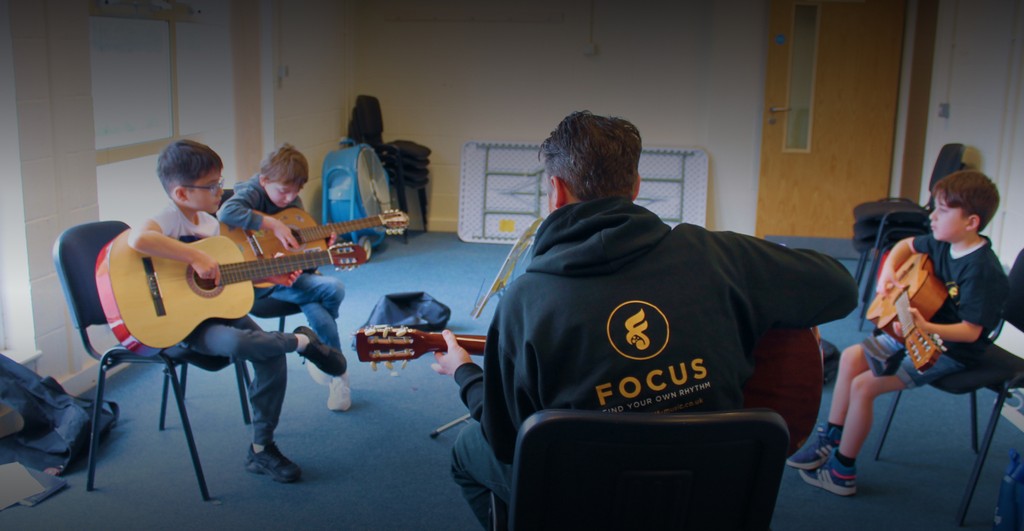 Students in the classroom being guided by the guitar teacher