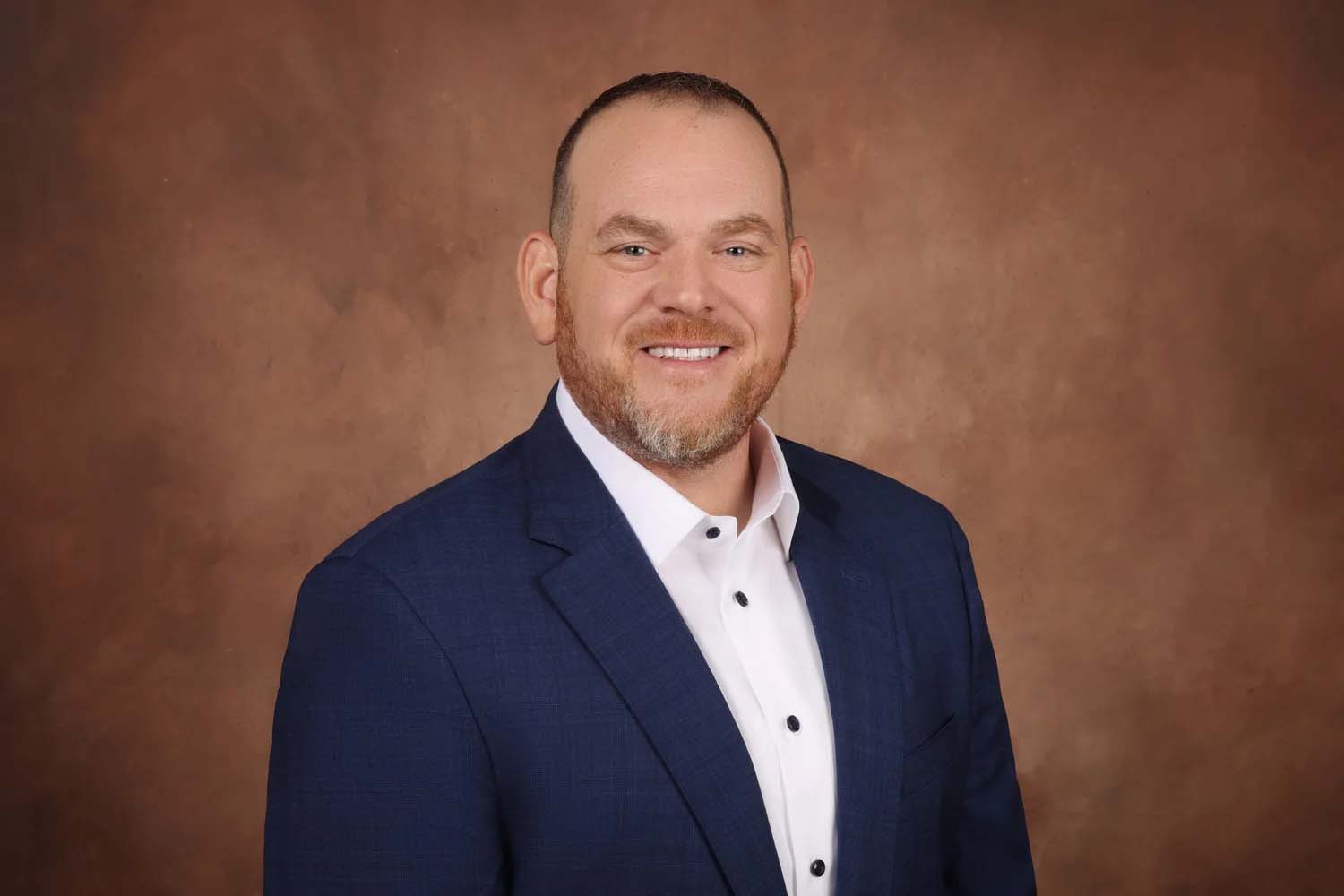 Studio portrait of a person smiling against a warm brown backdrop