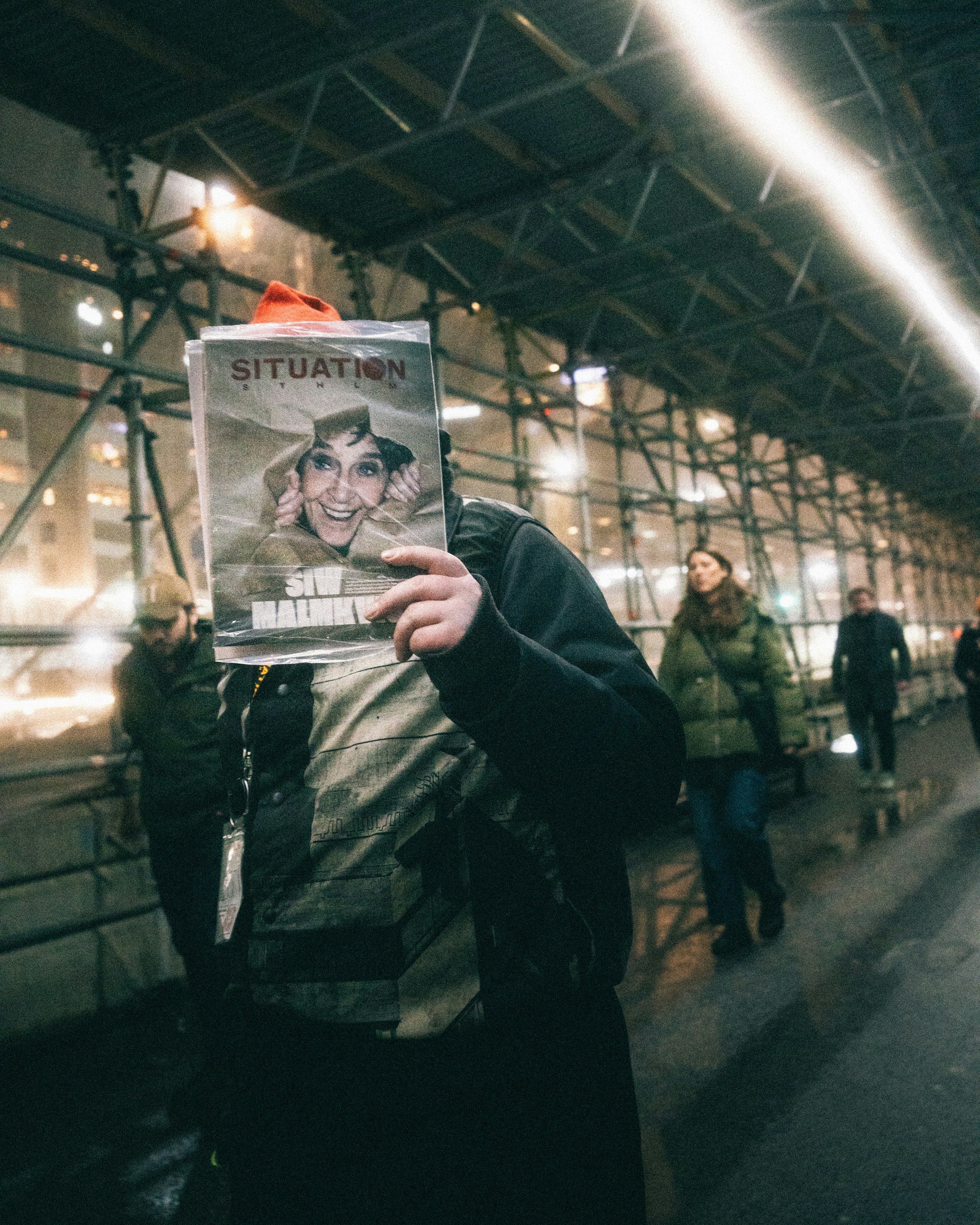 Person holds magazine covering face in public walkway