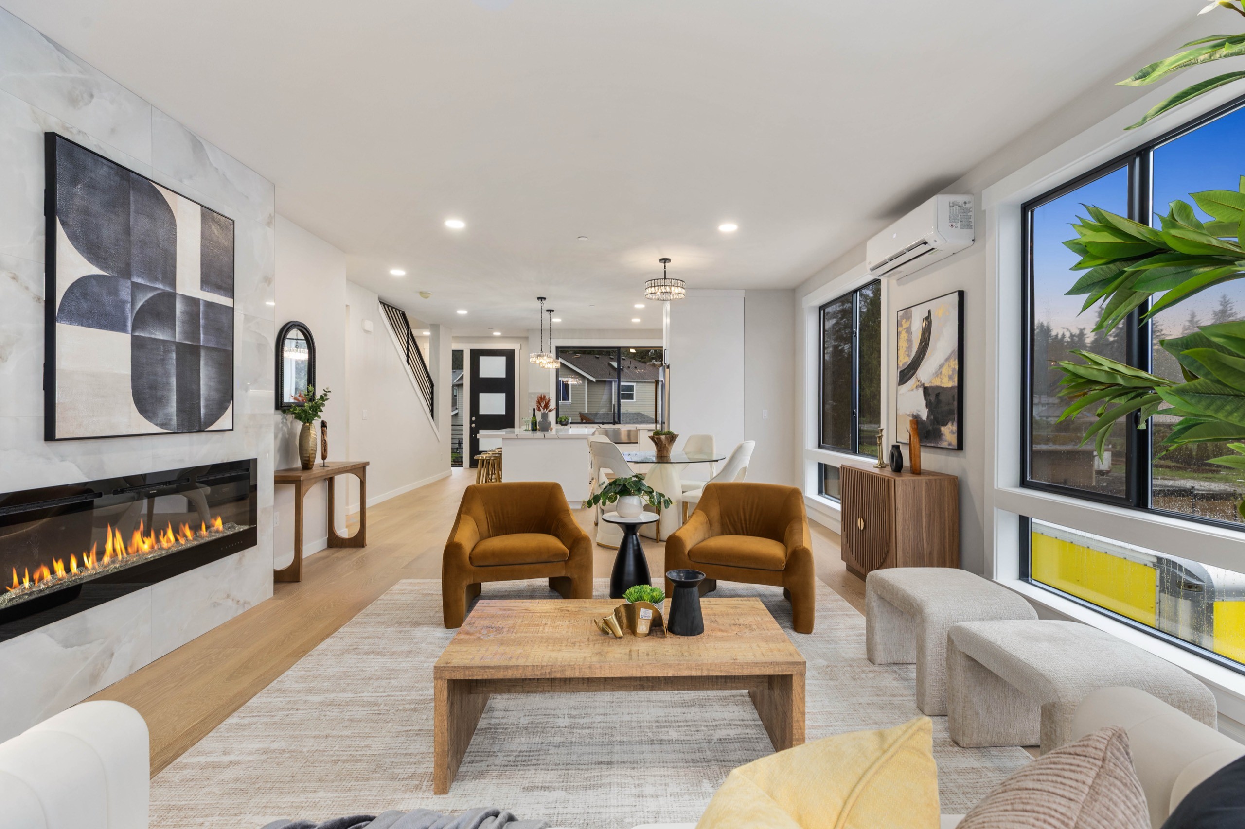Bright luxury living room with floor-to-ceiling windows, modern electric fireplace, hardwood floors, and open city views in a high-end residential home