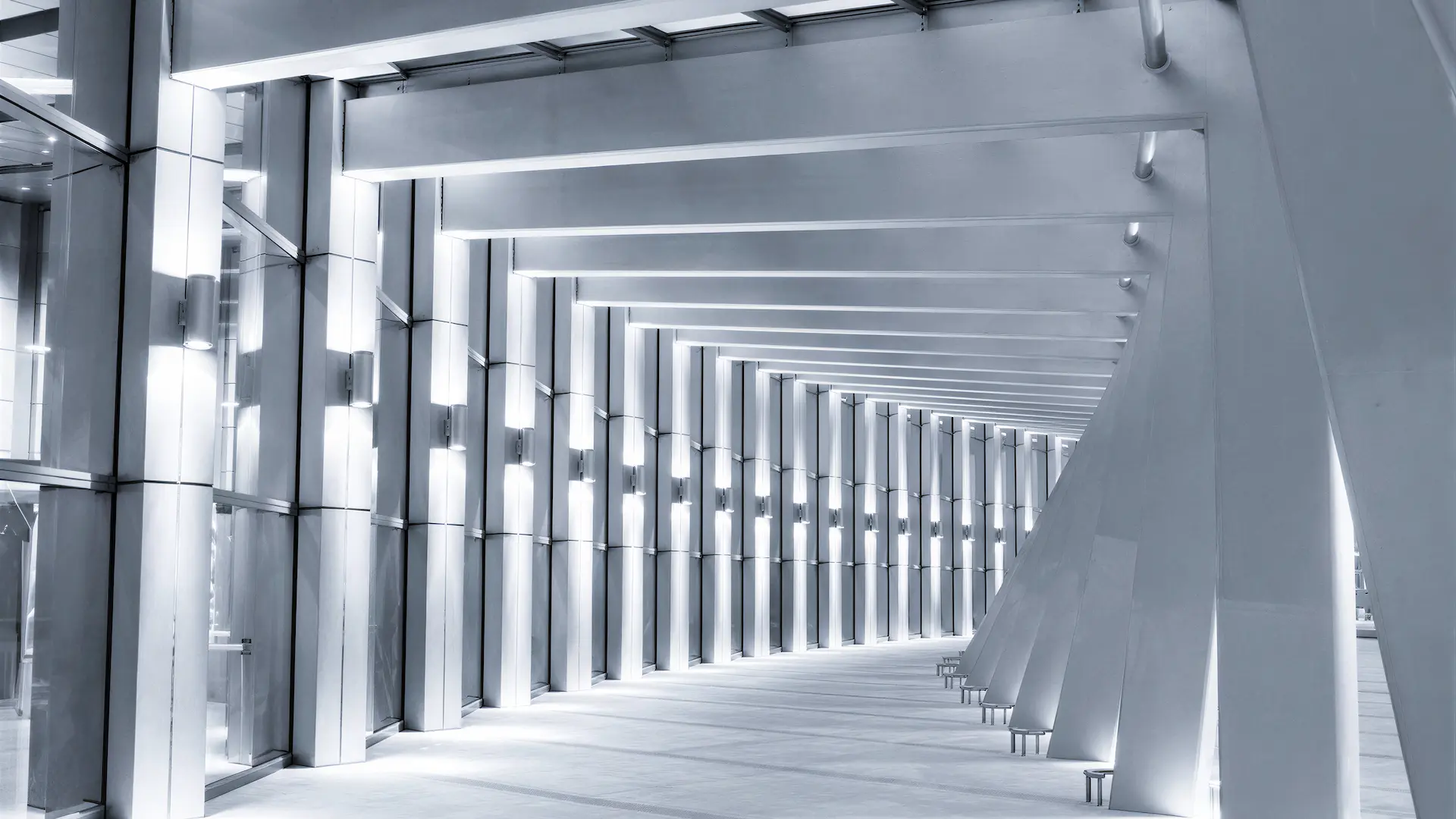 Modern corridor with exposed steel beams, structural columns, and illuminated vertical panels.