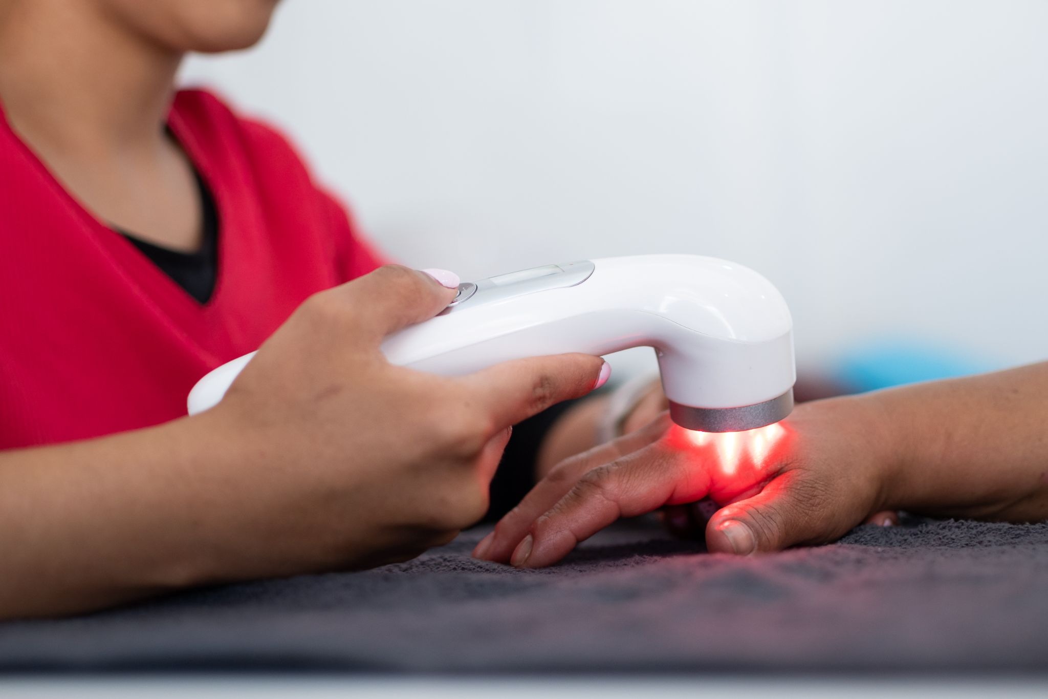 A close-up of a practitioner holding a handheld laser device that emits a red light onto a patient's hand during a therapy session.