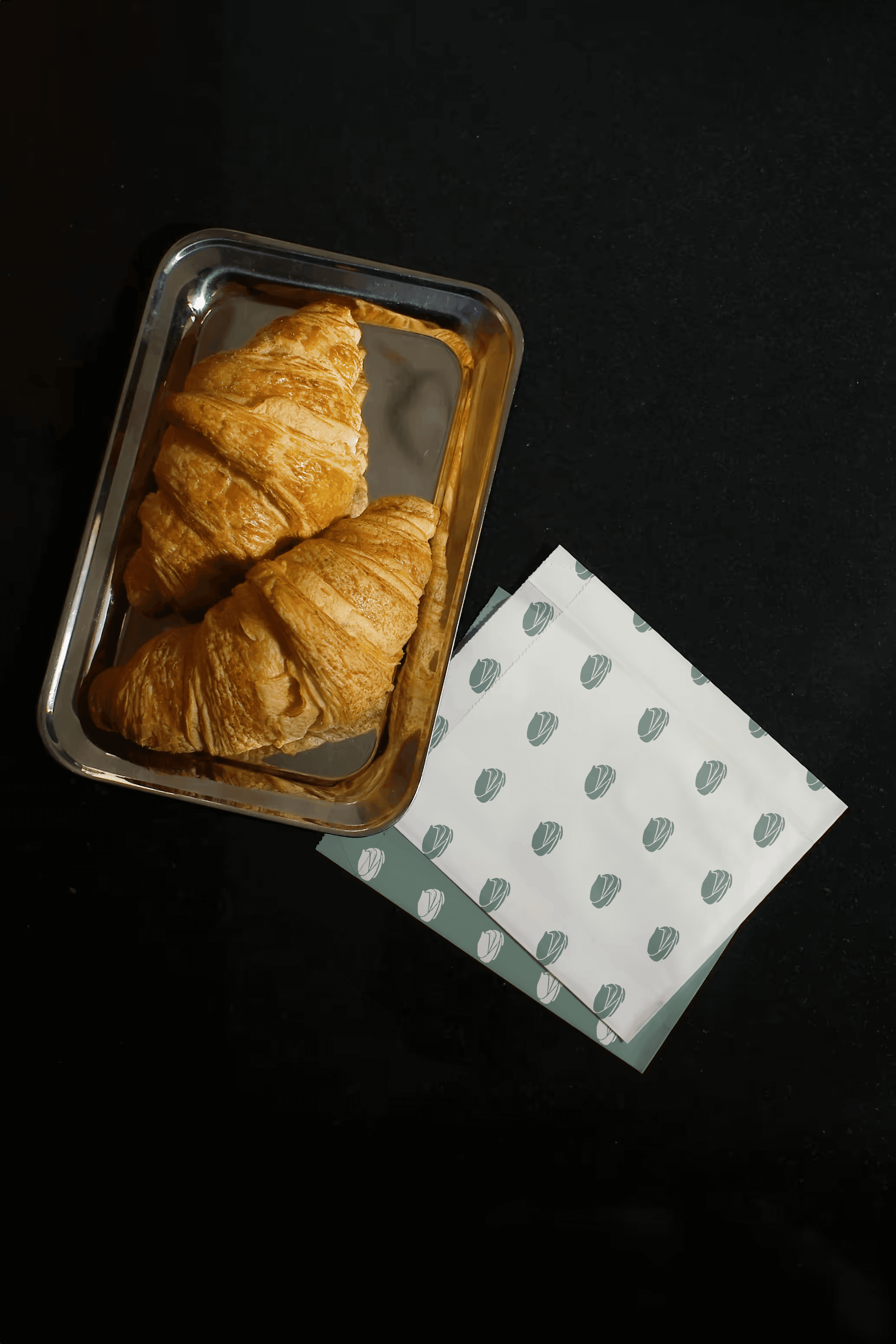 coastal sage mockup with a croissant and the brandmark in a repeating pattern on pastry bags