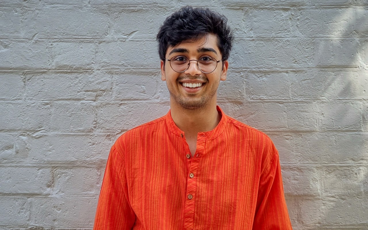 portrait of a smiling man with glasses. White brick wall in background