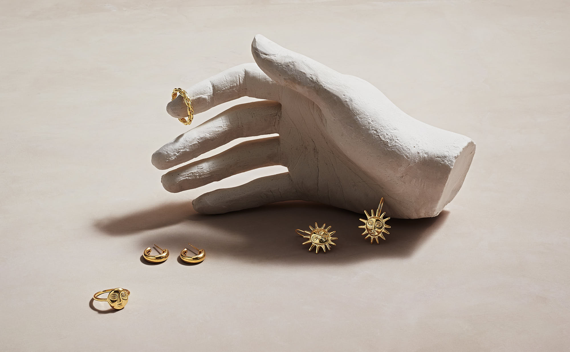 Gold jewelry set displayed on a plaster hand with sun-shaped earrings and rings.
