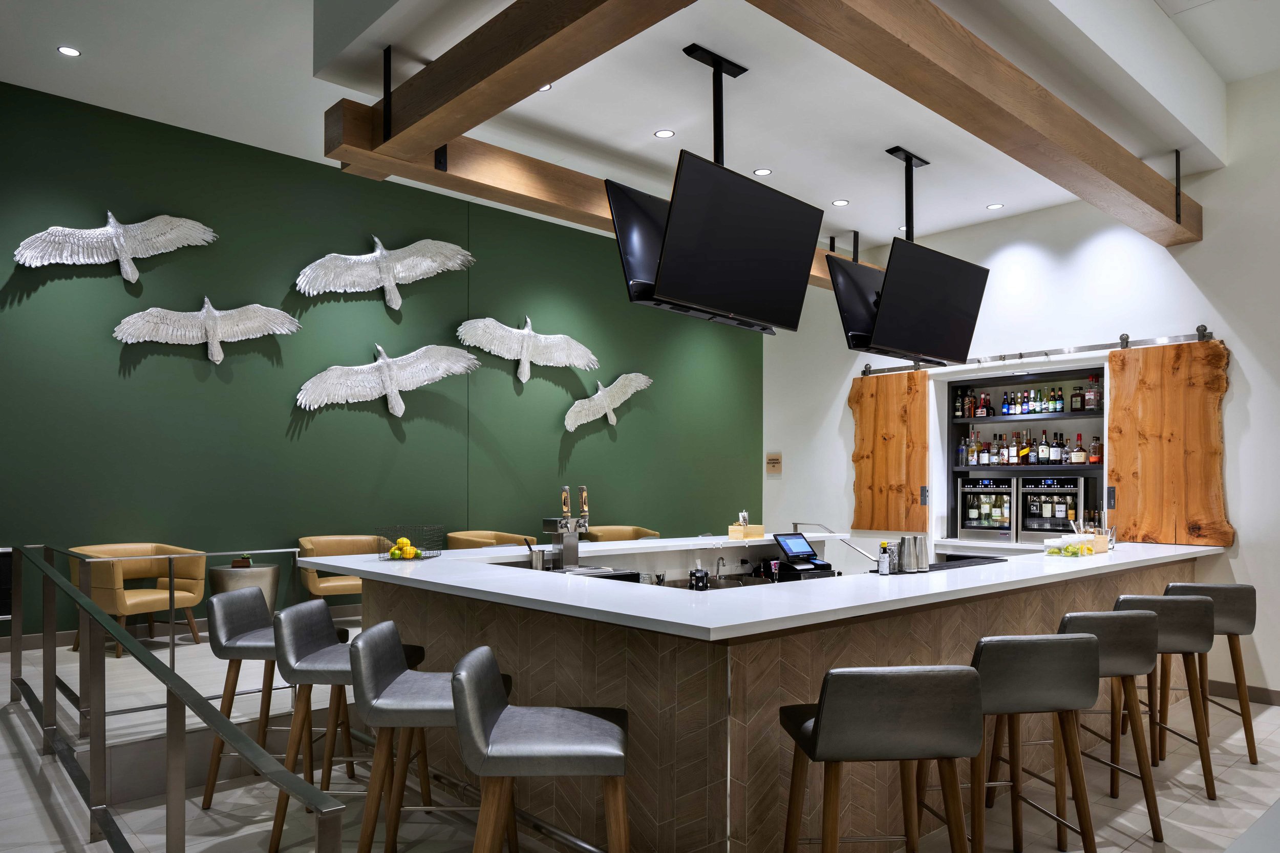 Bar with hanging TVs & flying bird decor on green wall.