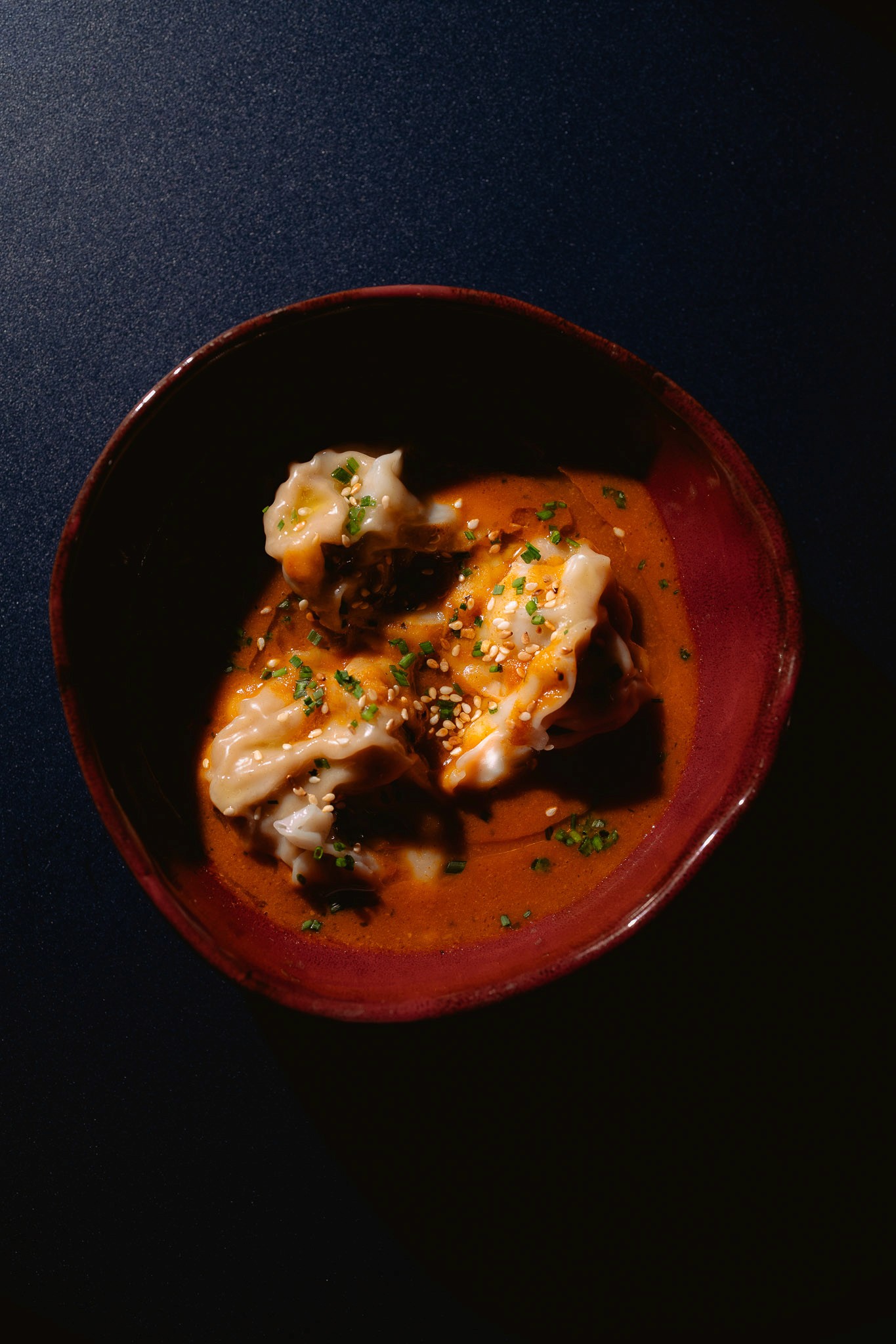 White plate with roasted carrots served on green sauce, topped with almonds and fresh herbs, held by a hand over a dark table.
