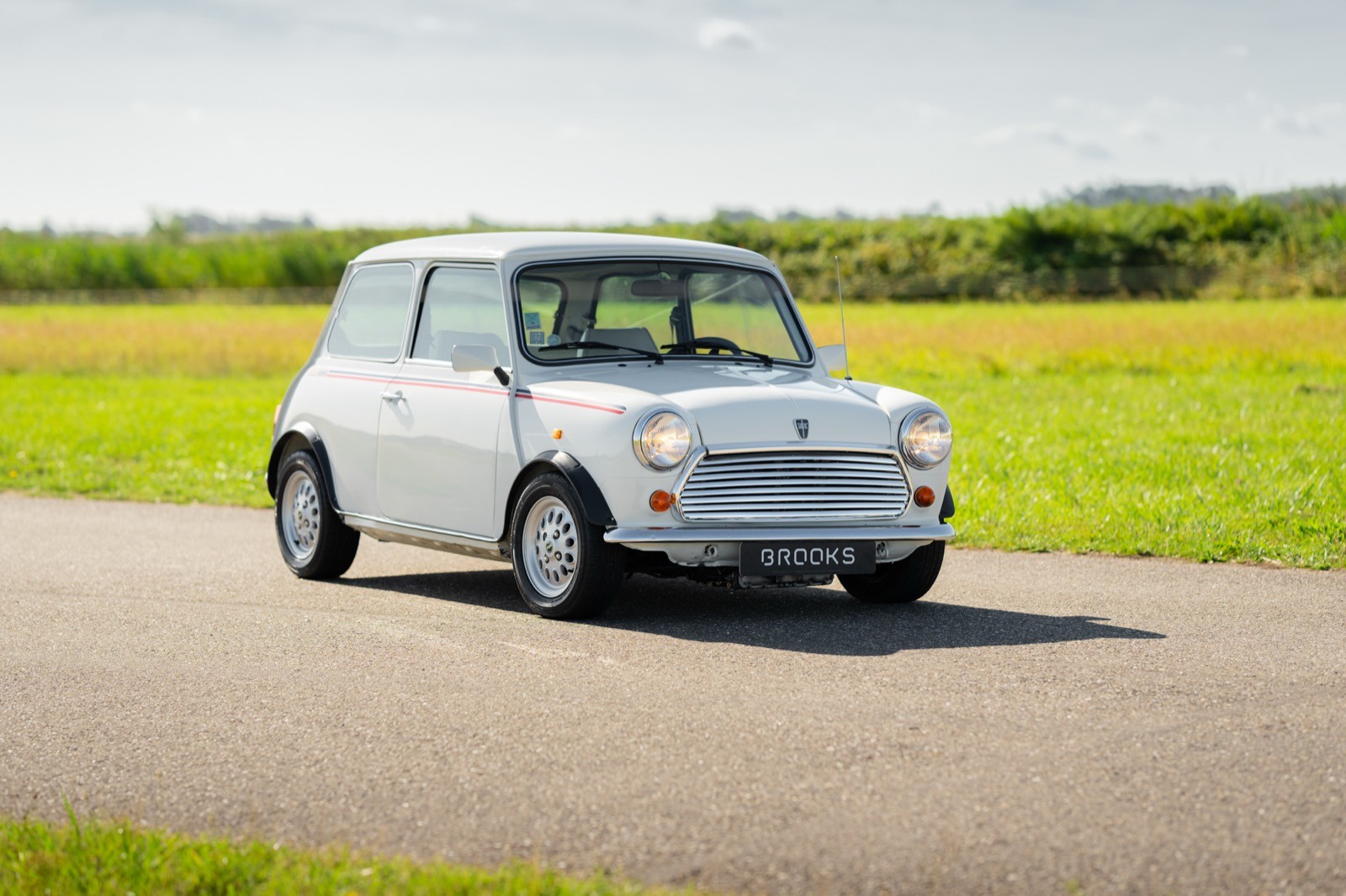 A small white car parked on a road with green fields in the background under a clear blue sky.