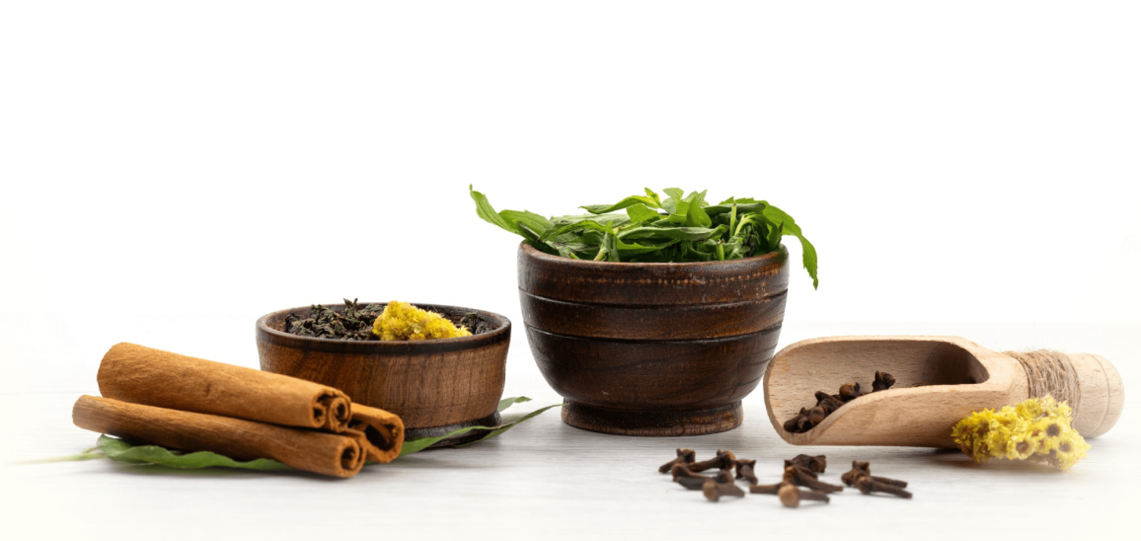 The image features a wooden bowl filled with fresh green herbs, cinnamon sticks, cloves, and dried flowers, representing natural spices and ingredients used in Ayurvedic diet consultation in Louisville.