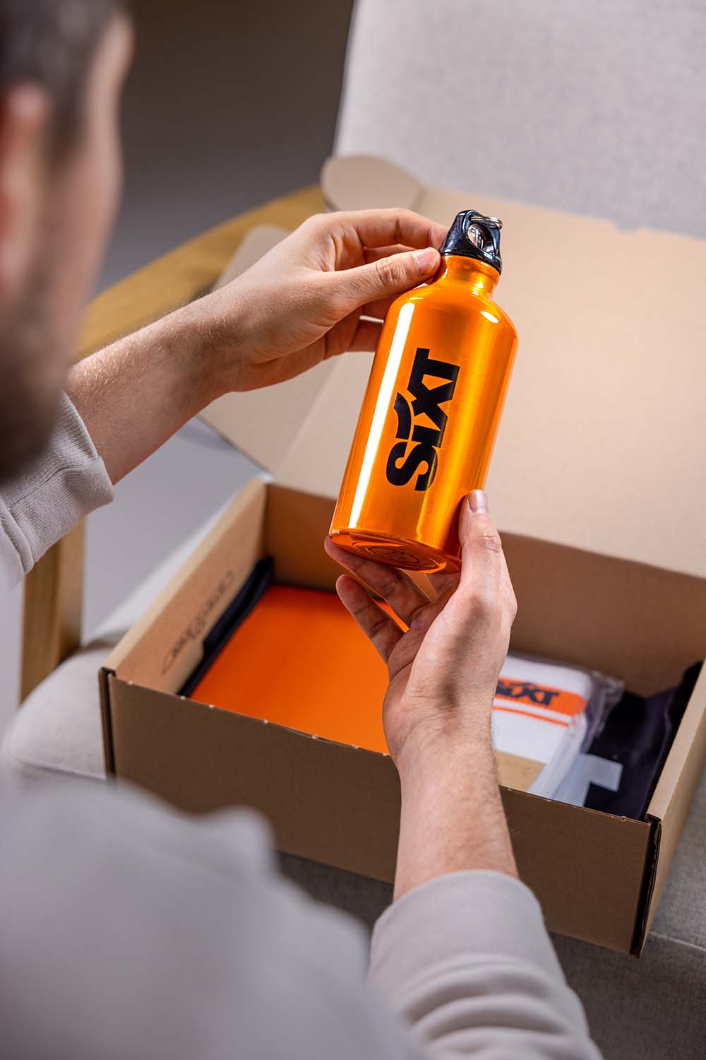 A person holds an orange bottle, examining it while looking inside an open cardboard box.
